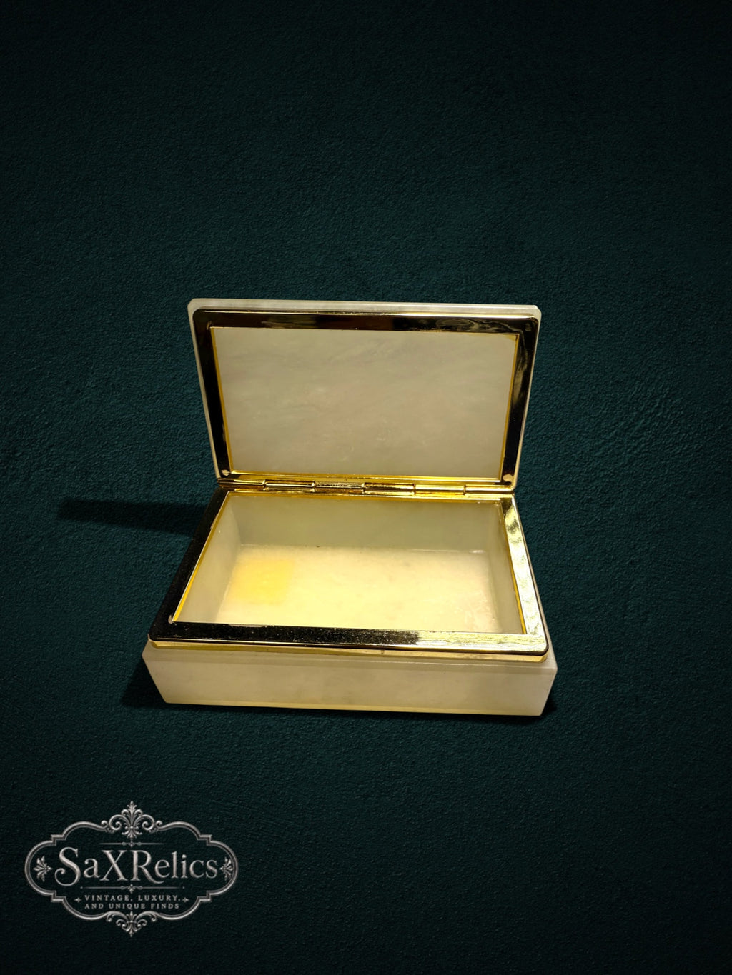 Alabaster trinket box with a polished gold-tone metal trim, shown open against a dark green background.