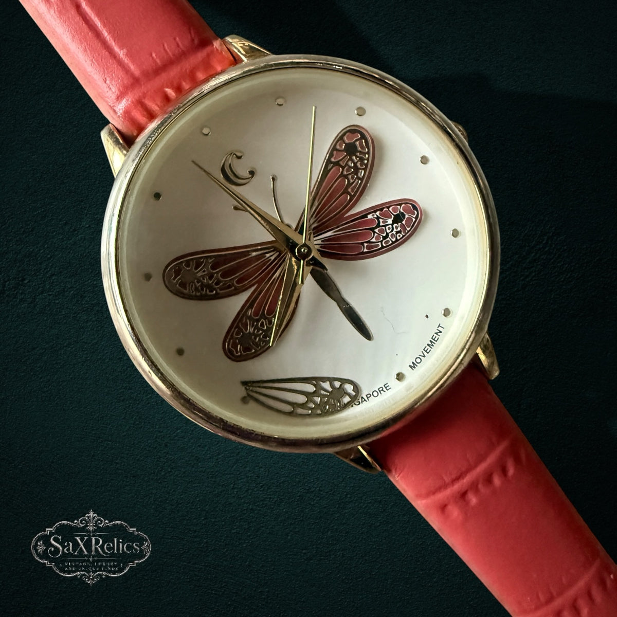 My Store analog wristwatch with a white dial, dragonfly motif, gold-tone case, and coral-pink textured leather strap.