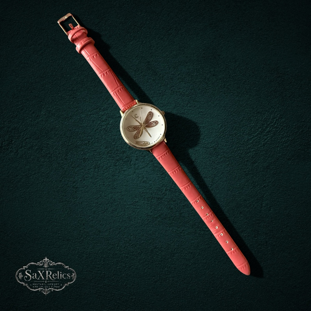 My Store analog wristwatch with a white dial, dragonfly motif, gold-tone case, and textured coral-pink leather strap.