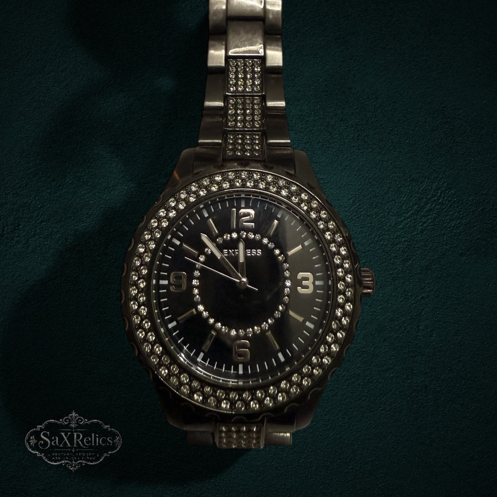 My Store Express dark metal link wristwatch with a crystal-encrusted bezel and black dial on a dark green background.