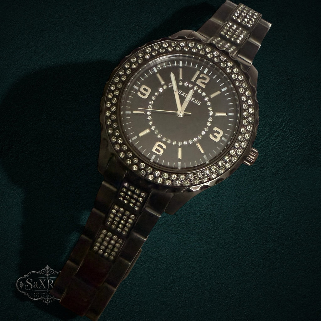 My Store EXPRESS dark metal link wristwatch with a crystal-encrusted bezel and black dial on a dark background