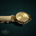 My Store Geneva analog wristwatch with a gold-tone round case and a cream-colored textured leather strap.