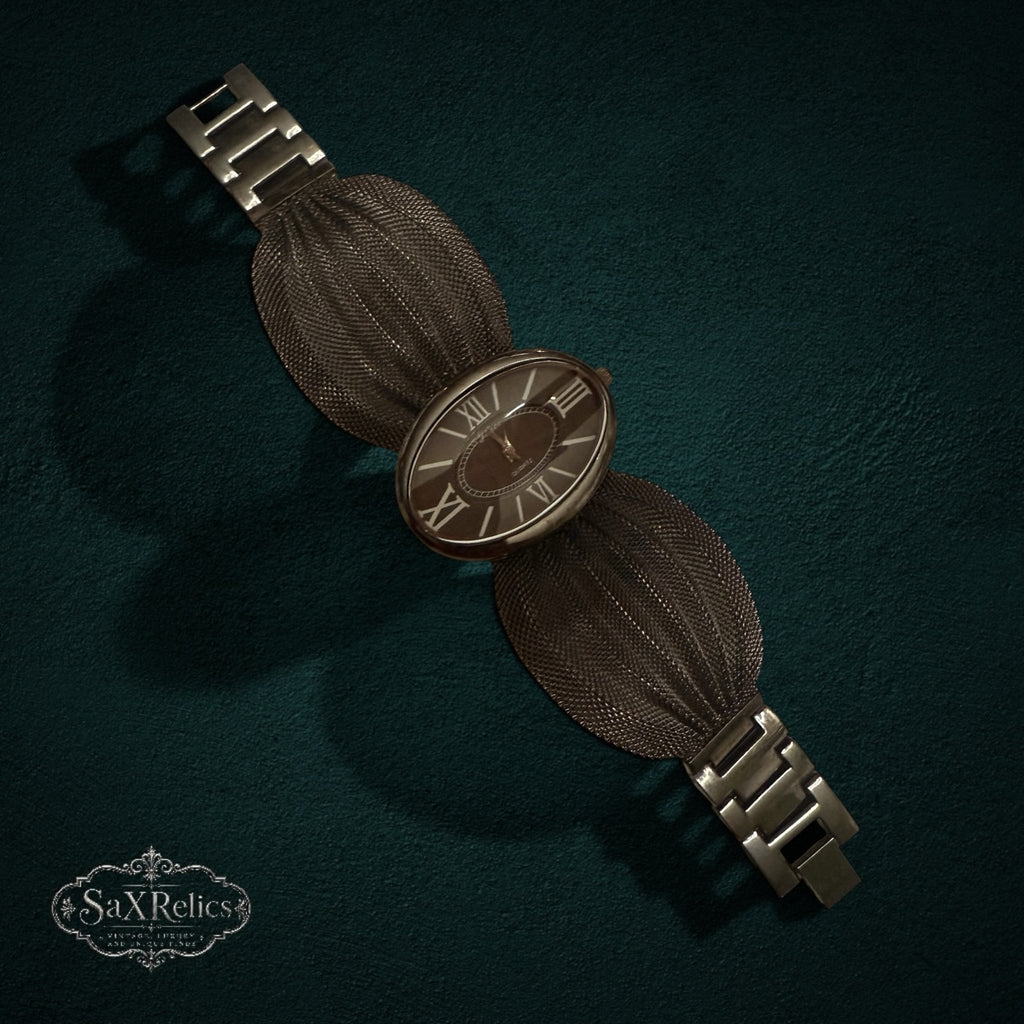 My Store Geneva quartz wristwatch with a dark metallic oval dial, Roman numerals, and a textured fan-like mesh bracelet.