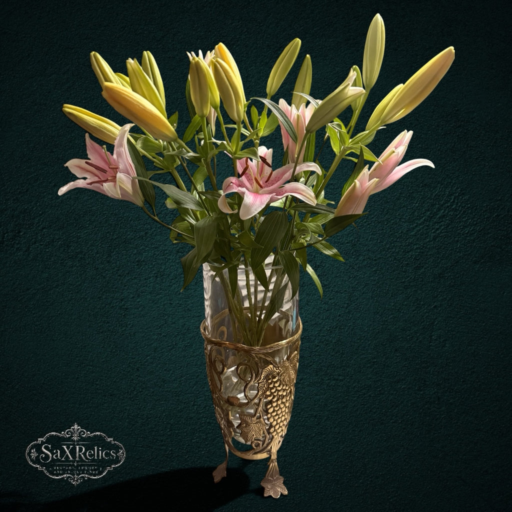 My Store SAXRelics glass flower vase in an ornate brass-tone metal stand with grape and vine motifs holding lilies.