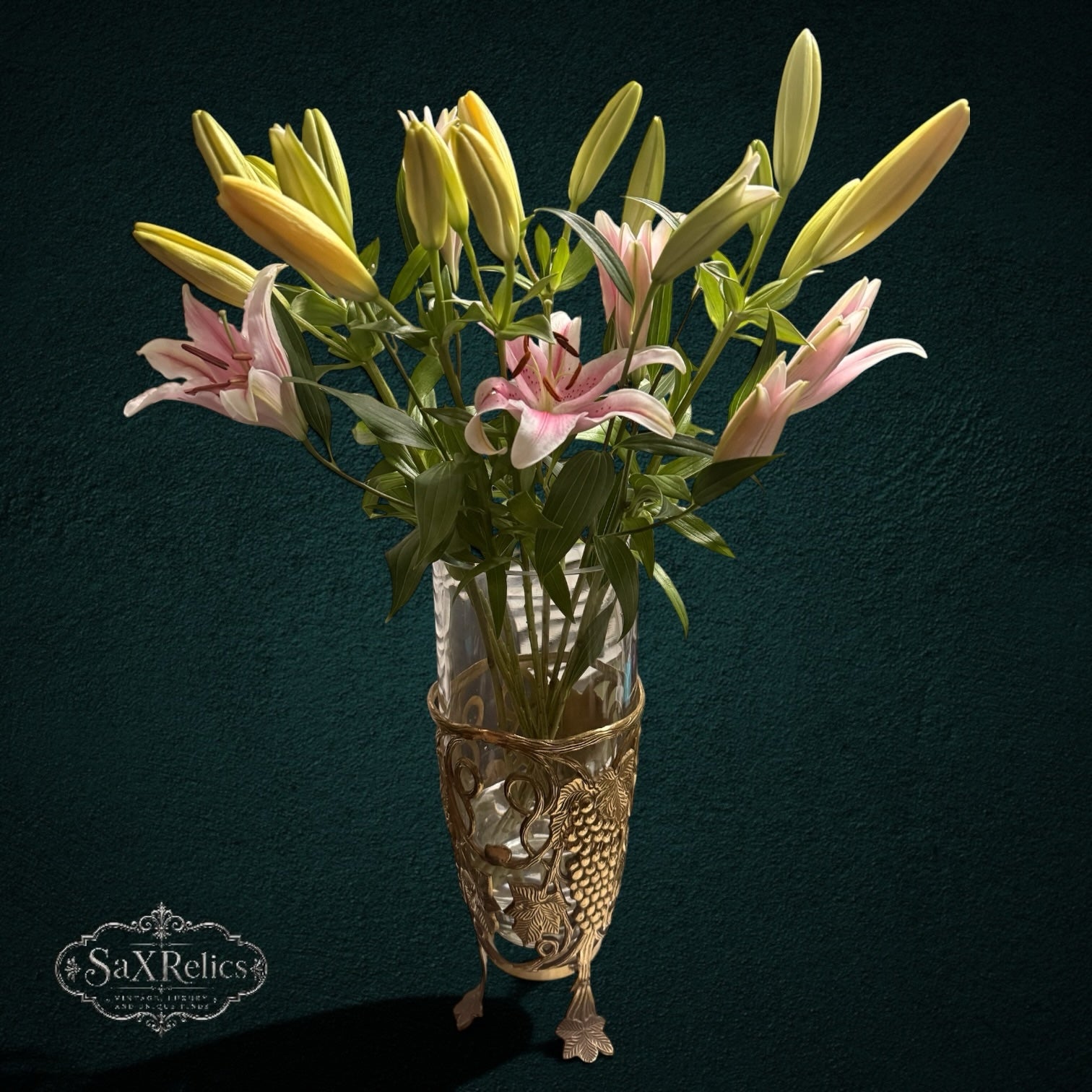 My Store SAXRelics glass flower vase in an ornate brass-tone metal stand with grape and vine motifs holding lilies.