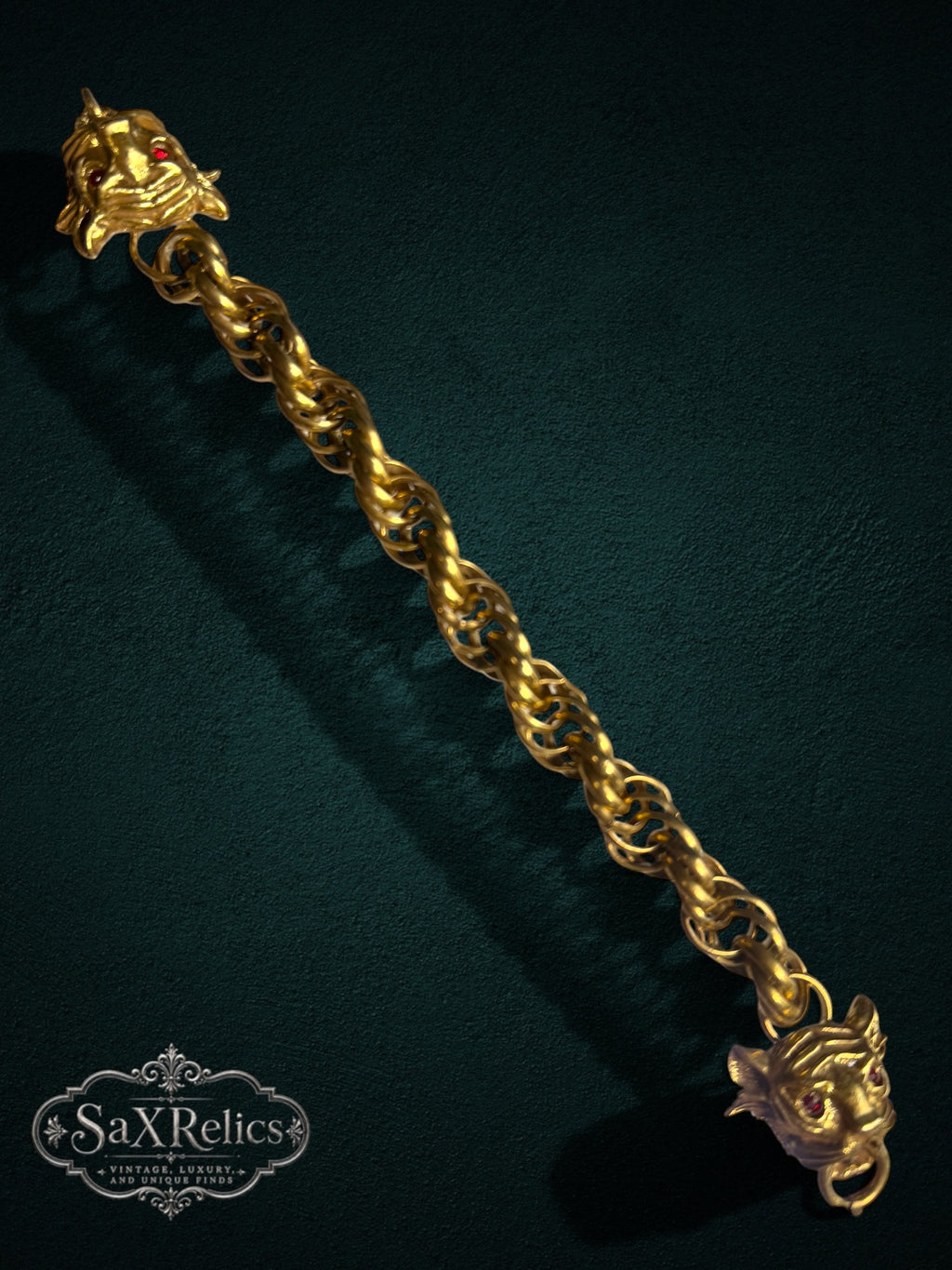SaX Relics gold-tone link bracelet featuring dual lion heads with red gemstone eyes on a dark textured background