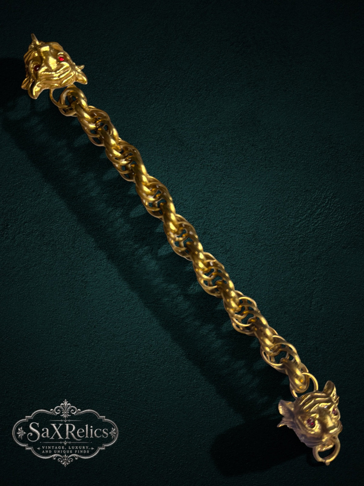 SaX Relics gold-tone link bracelet featuring dual lion heads with red gemstone eyes on a dark textured background