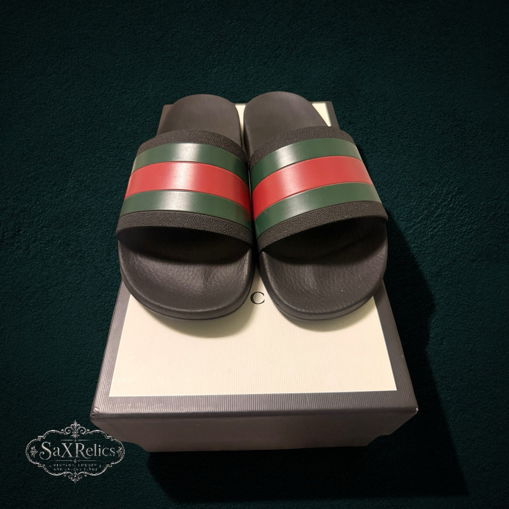 My Store GUCCI rubber slide sandals in black with iconic green and red web stripe detail resting on a branded box.
