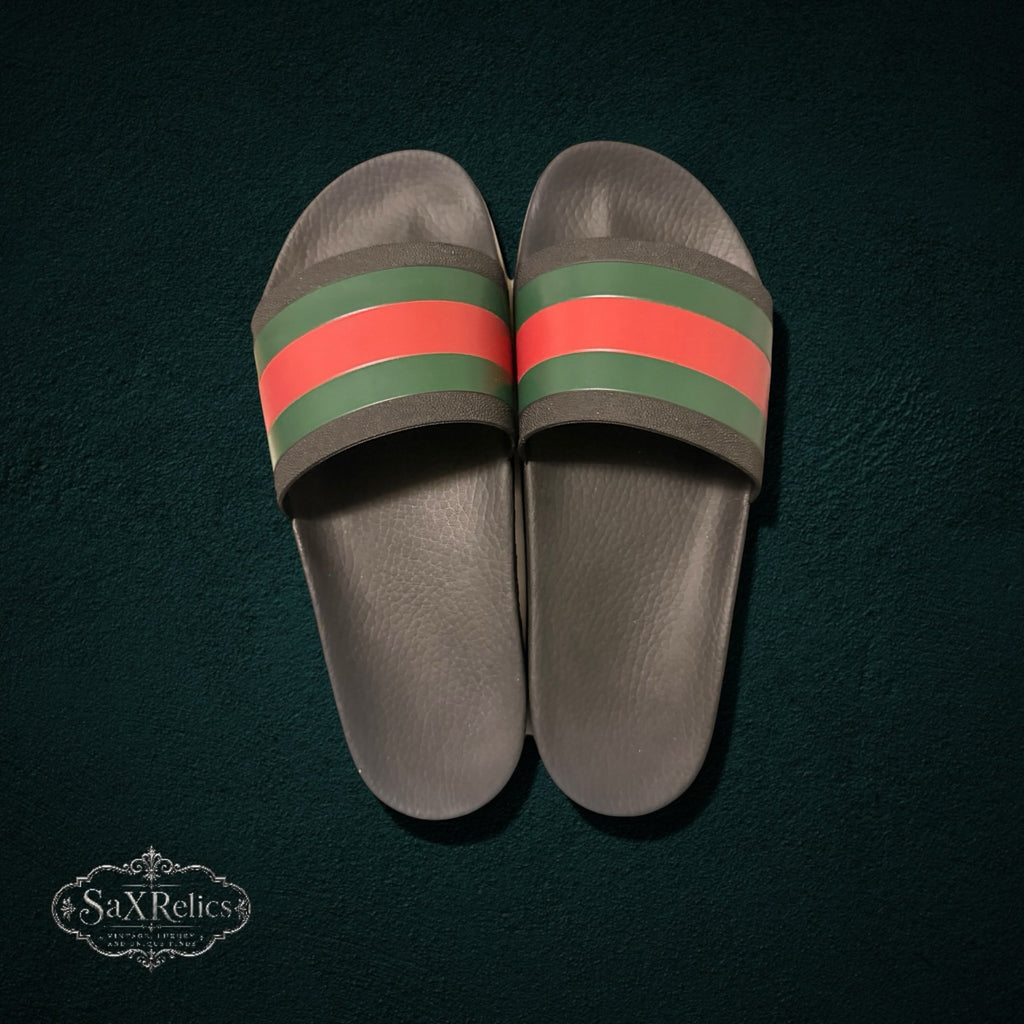 My Store Gucci rubber slide sandals in black with signature green and red web stripe detail on a dark textured background