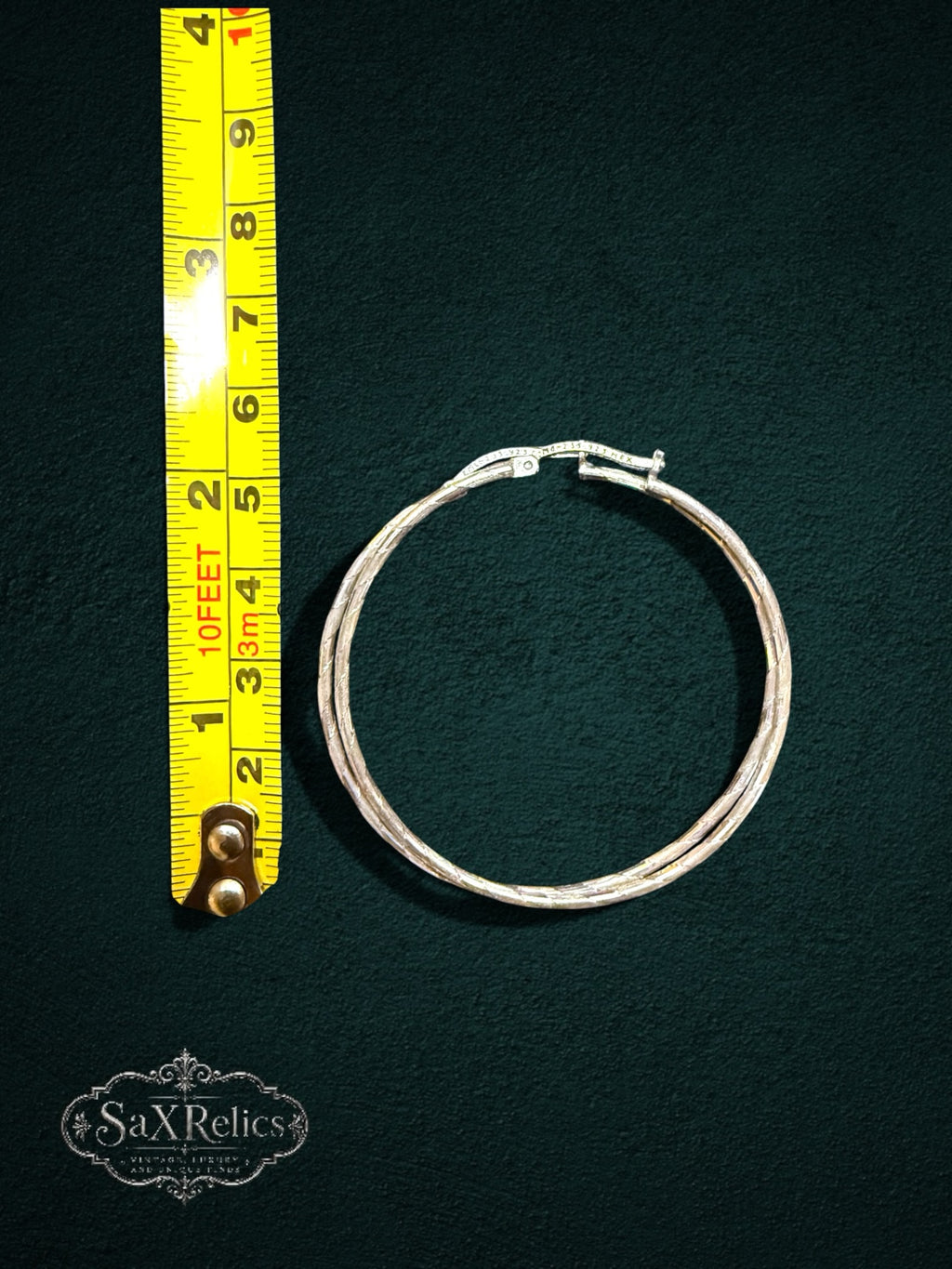 My Store large sterling silver hoop earrings with a textured finish and hinged closure measured against a yellow tape.
