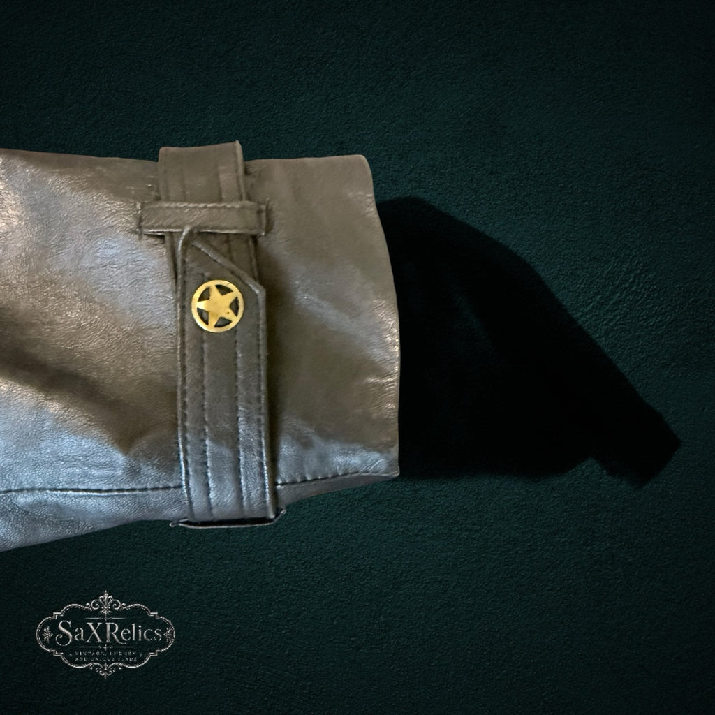 Metallic silver-grey leather jacket sleeve featuring a gold-tone star-embossed button and cuff strap detail.