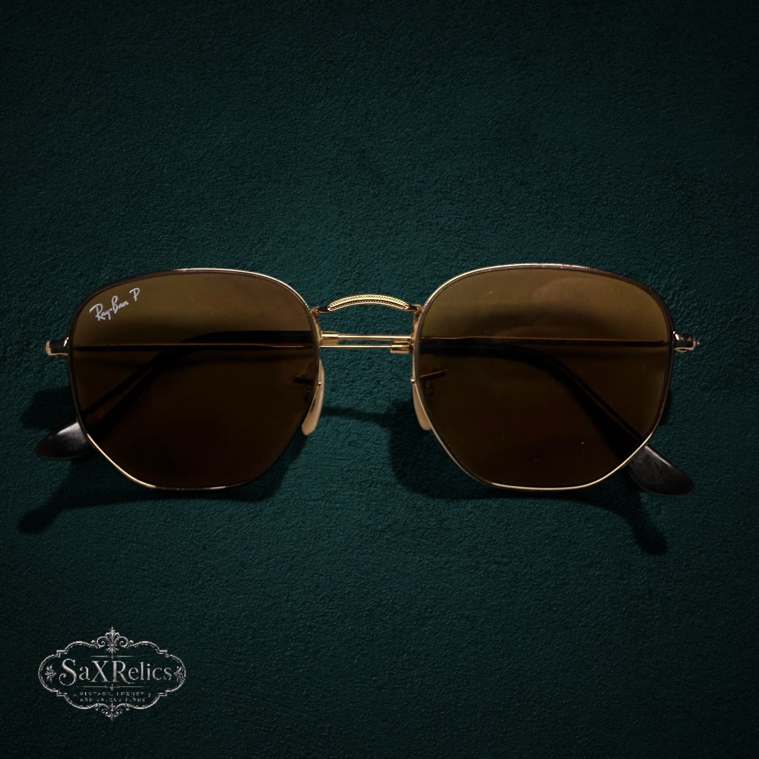 My Store Ray-Ban polarized sunglasses with a gold-tone geometric metal frame on a dark green textured background.