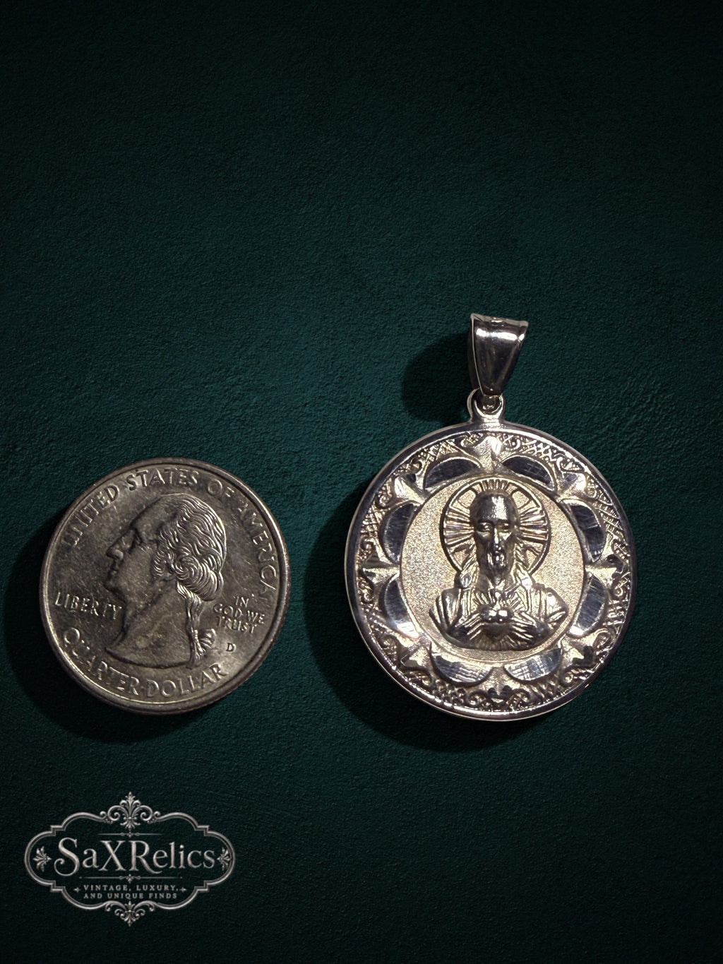 Religious pendant featuring the Sacred Heart of Jesus with an ornate border, shown next to a US quarter.