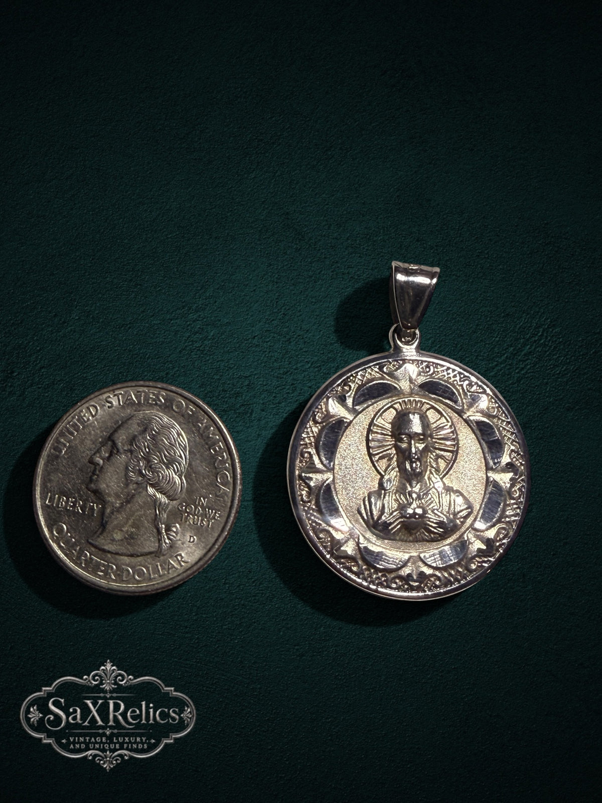 Religious pendant featuring the Sacred Heart of Jesus with an ornate border, shown next to a US quarter.