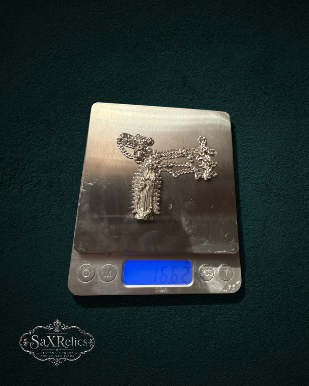 My Store SaxRelics silver-tone Our Lady of Guadalupe pendant necklace with curb chain on a digital scale