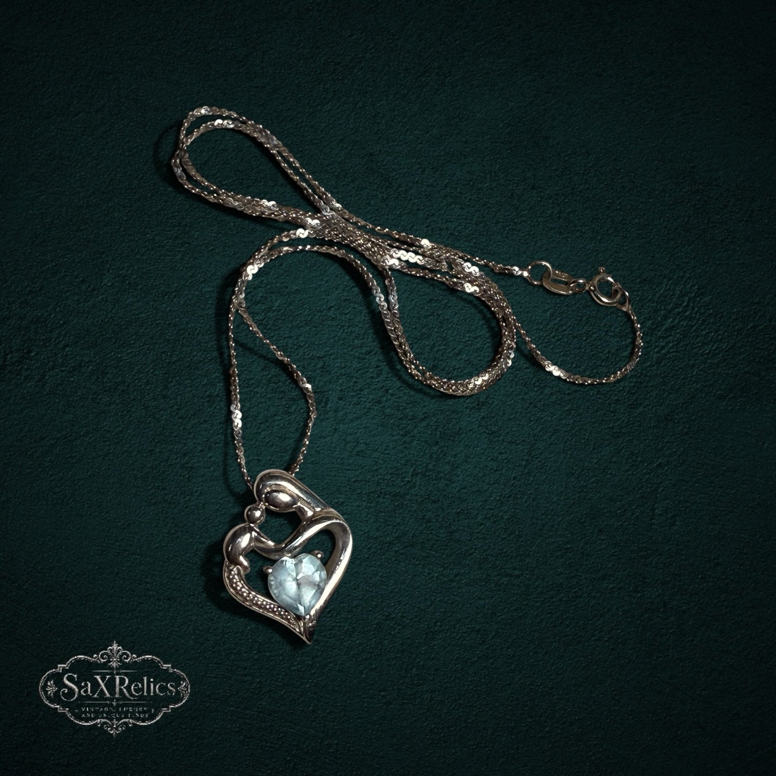 My Store SAXRelics sterling silver mother and child heart pendant necklace with a light blue heart-cut gemstone.