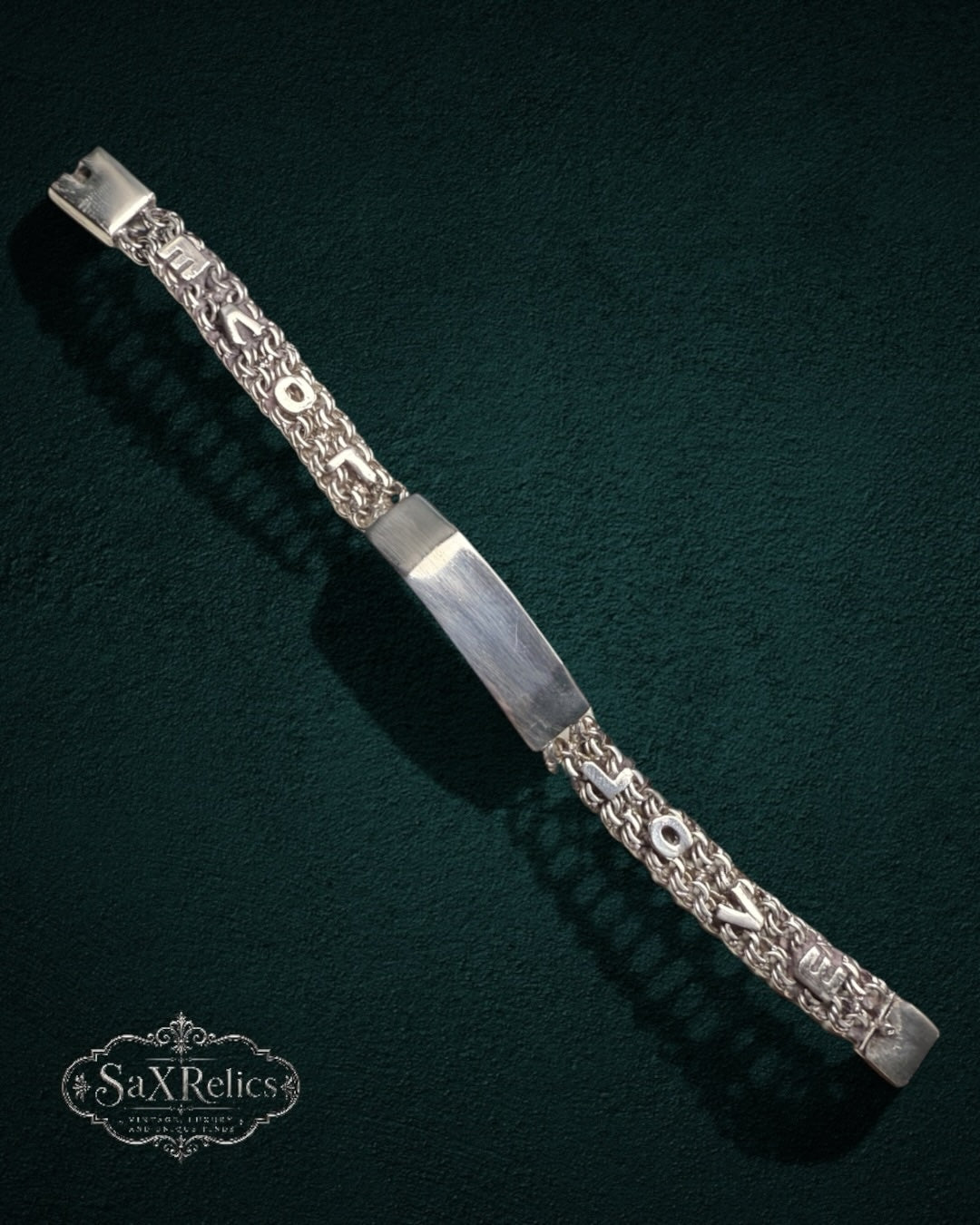 My Store SAXRelics silver link chain bracelet with a polished identification plate and textured links on dark green