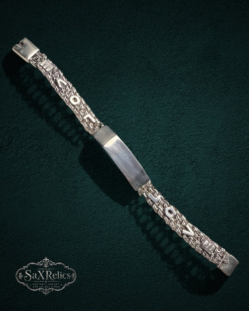 My Store SAXRelics silver link chain bracelet with a polished identification plate and textured links on dark green