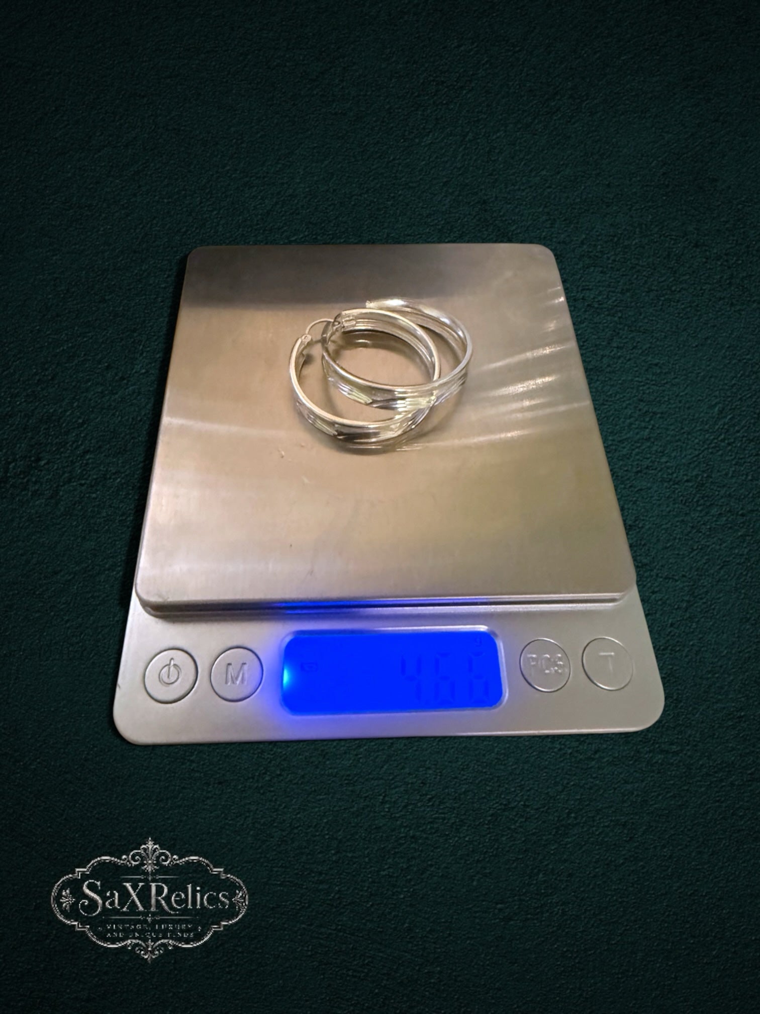 My Store SAXRelics polished sterling silver hoop earrings with etched texture resting on a digital scale