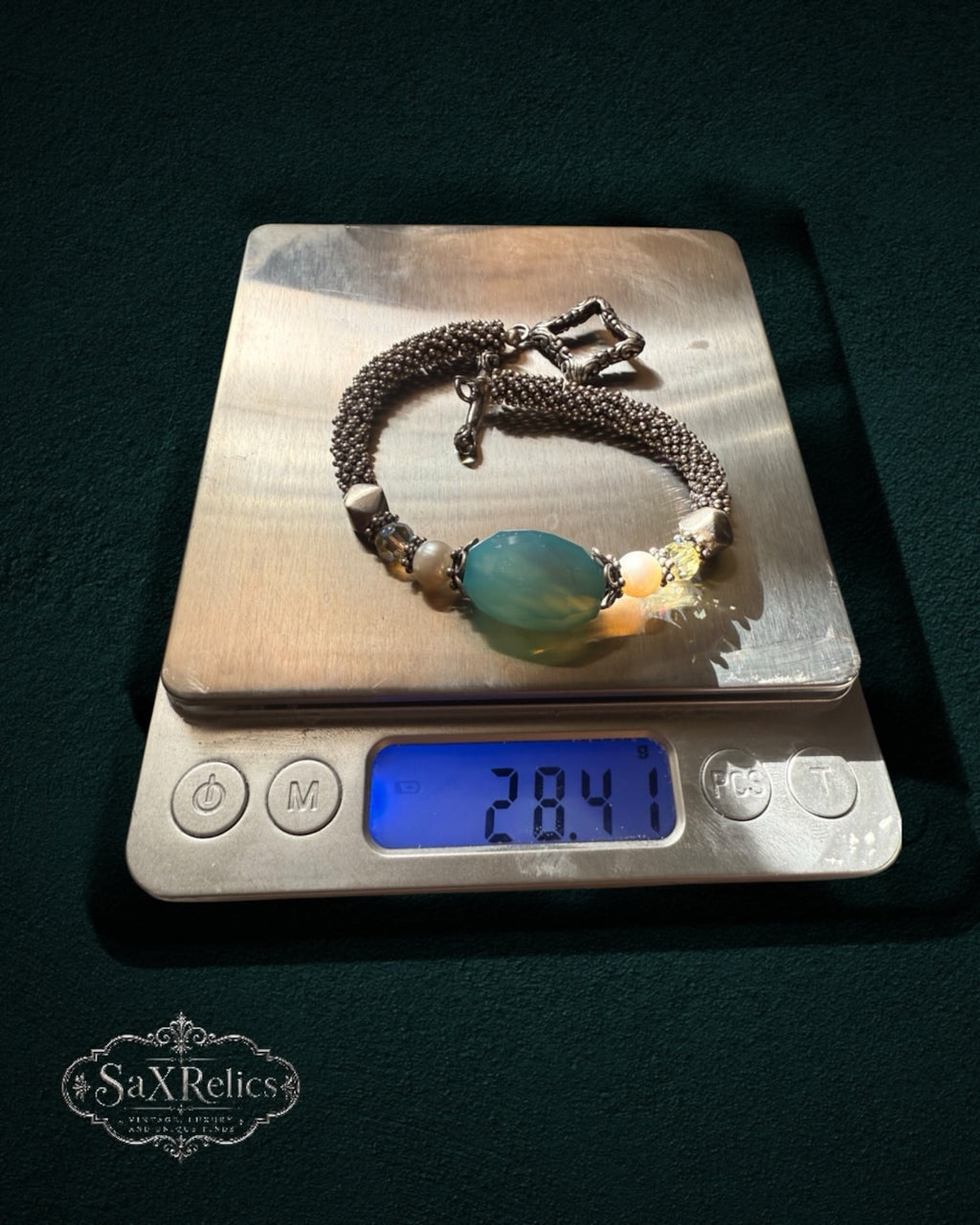My Store SaxRelics beaded bracelet with a teal gemstone, pearls, and silver mesh chain on a digital scale