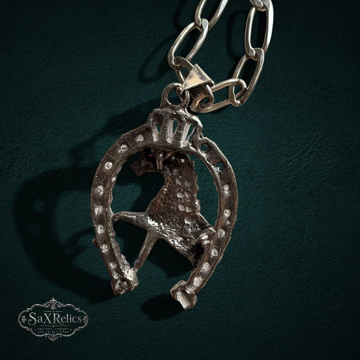 SaX Relics — Herradura pendant detail showing the horse head within the horseshoe frame and red CZ accent.