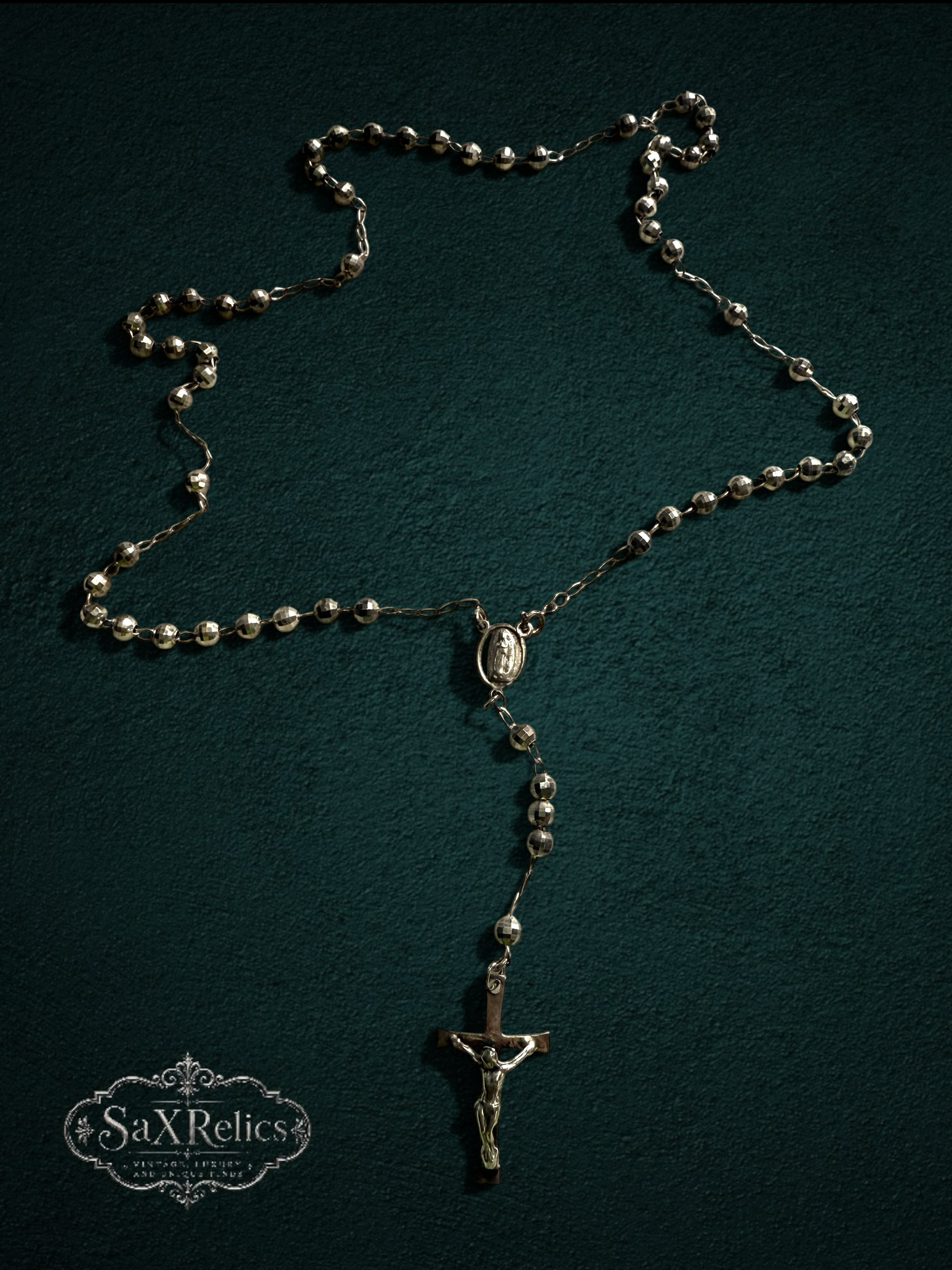 My Store silver-tone rosary necklace with faceted beads, centerpiece medal, and crucifix on a dark green background.