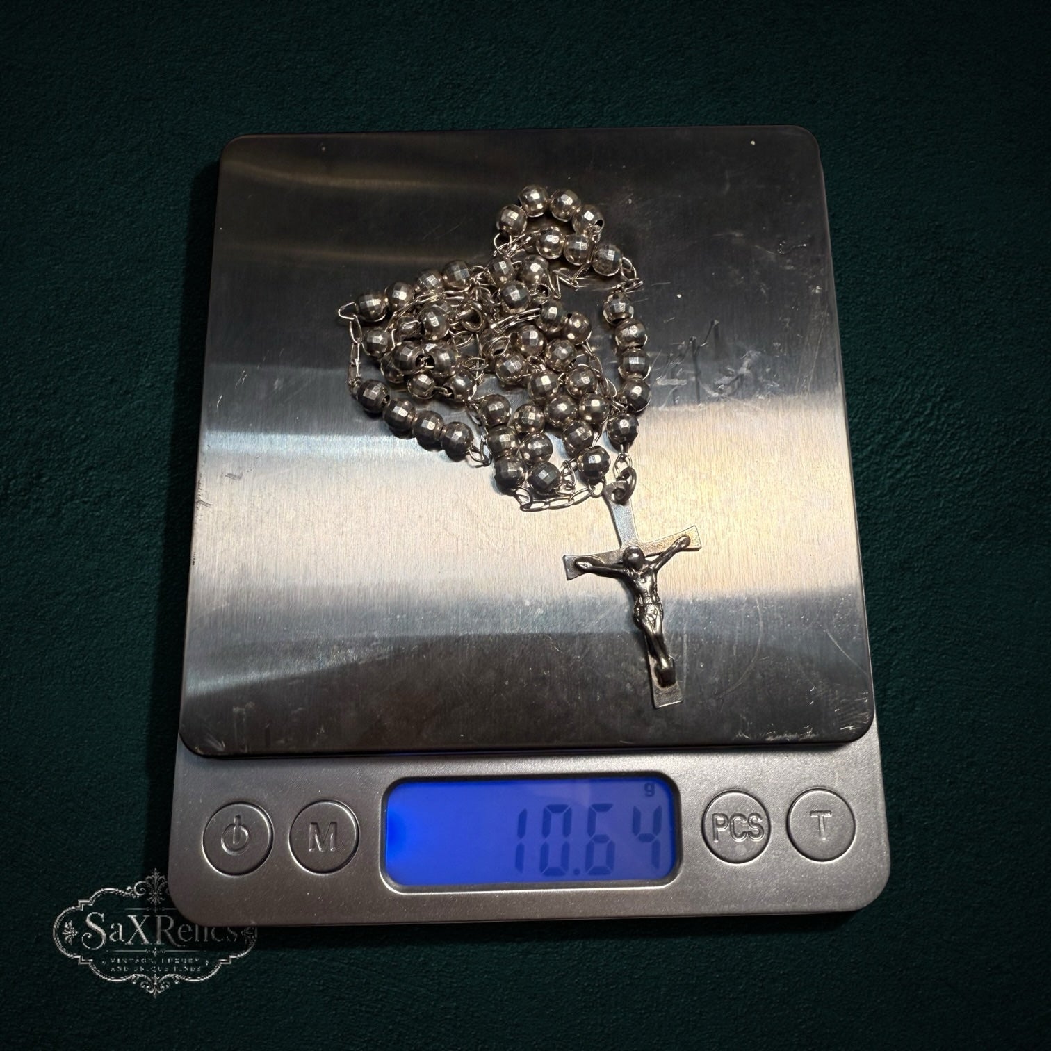 My Store silver-tone rosary beads with a detailed crucifix centerpiece resting on a digital scale weighing 10.64 grams.