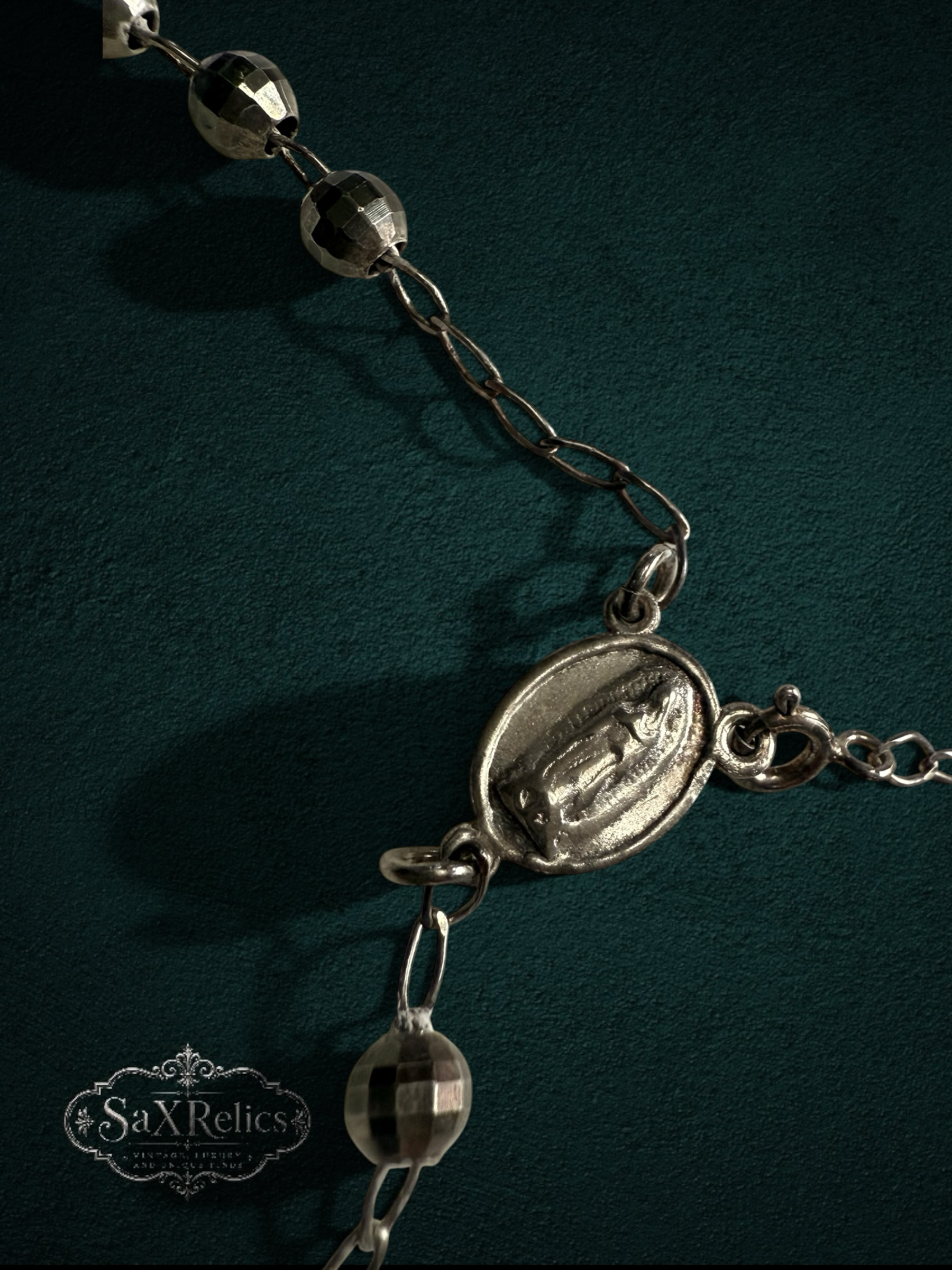 My Store silver-tone rosary necklace with faceted beads and a detailed religious centerpiece on a dark green background