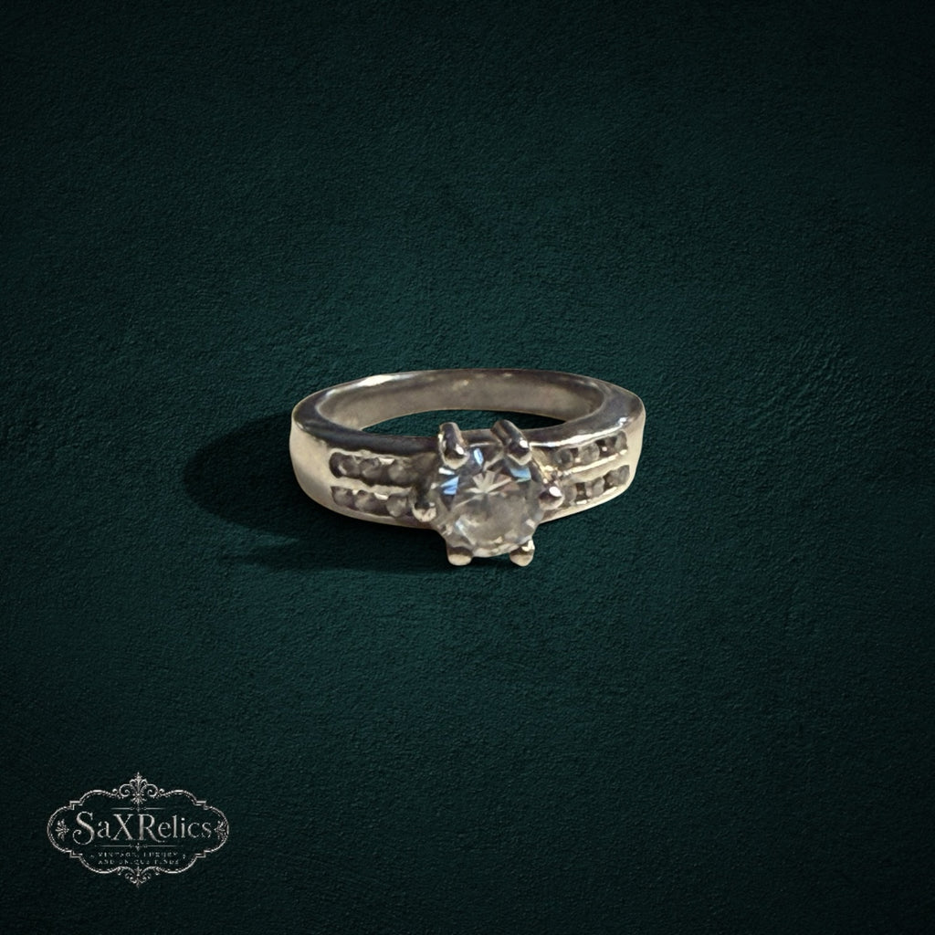 My Store silver-tone solitaire ring with a center stone and shimmering accent stones on a dark green background.