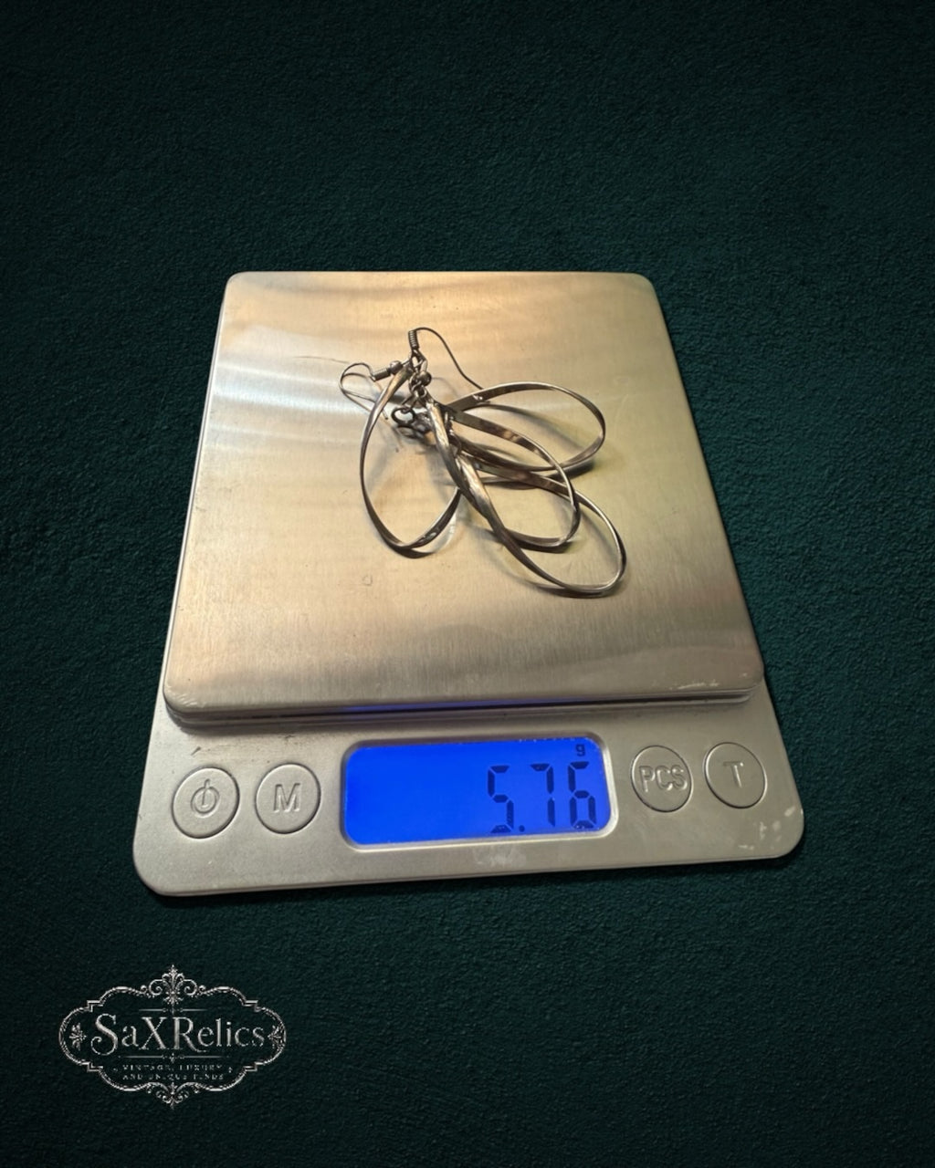 My Store silver-tone intertwined teardrop dangle earrings resting on a digital scale showing 5.76 grams