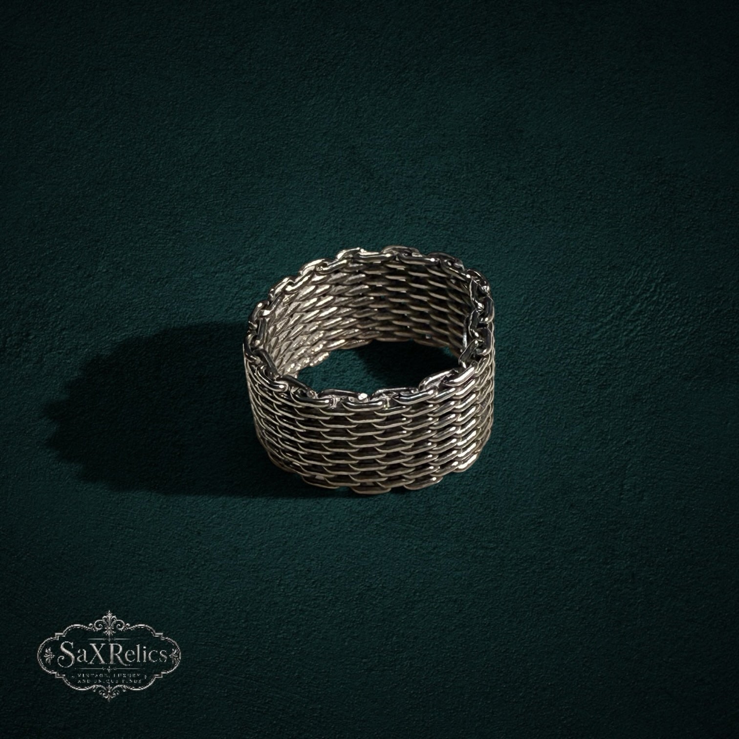 My Store SAXRelics silver-toned woven chain-link band ring with intricate chainmail texture on a dark green background.