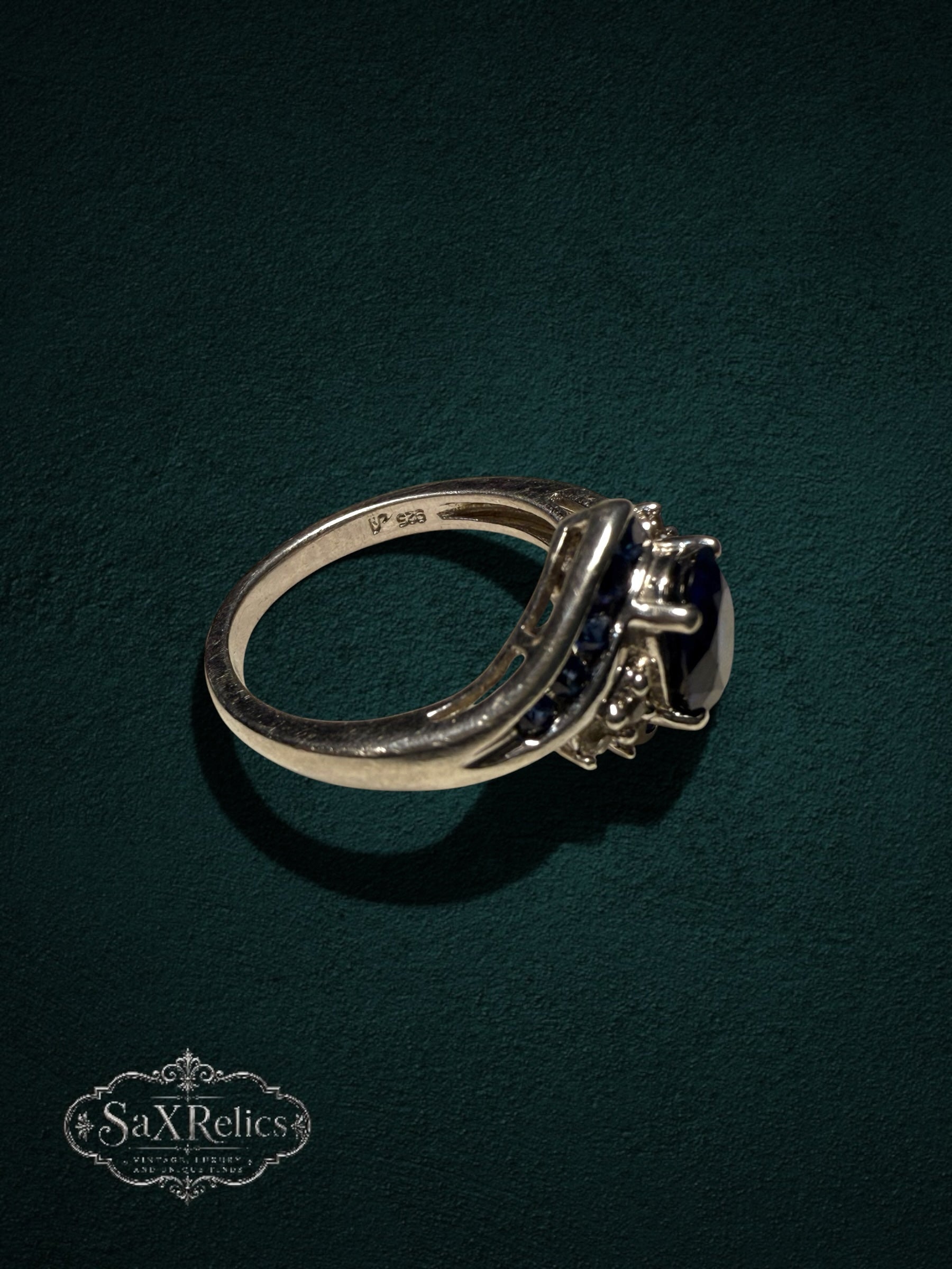 My Store sterling silver statement ring with a deep blue oval-cut center stone and crystal accents on a green background