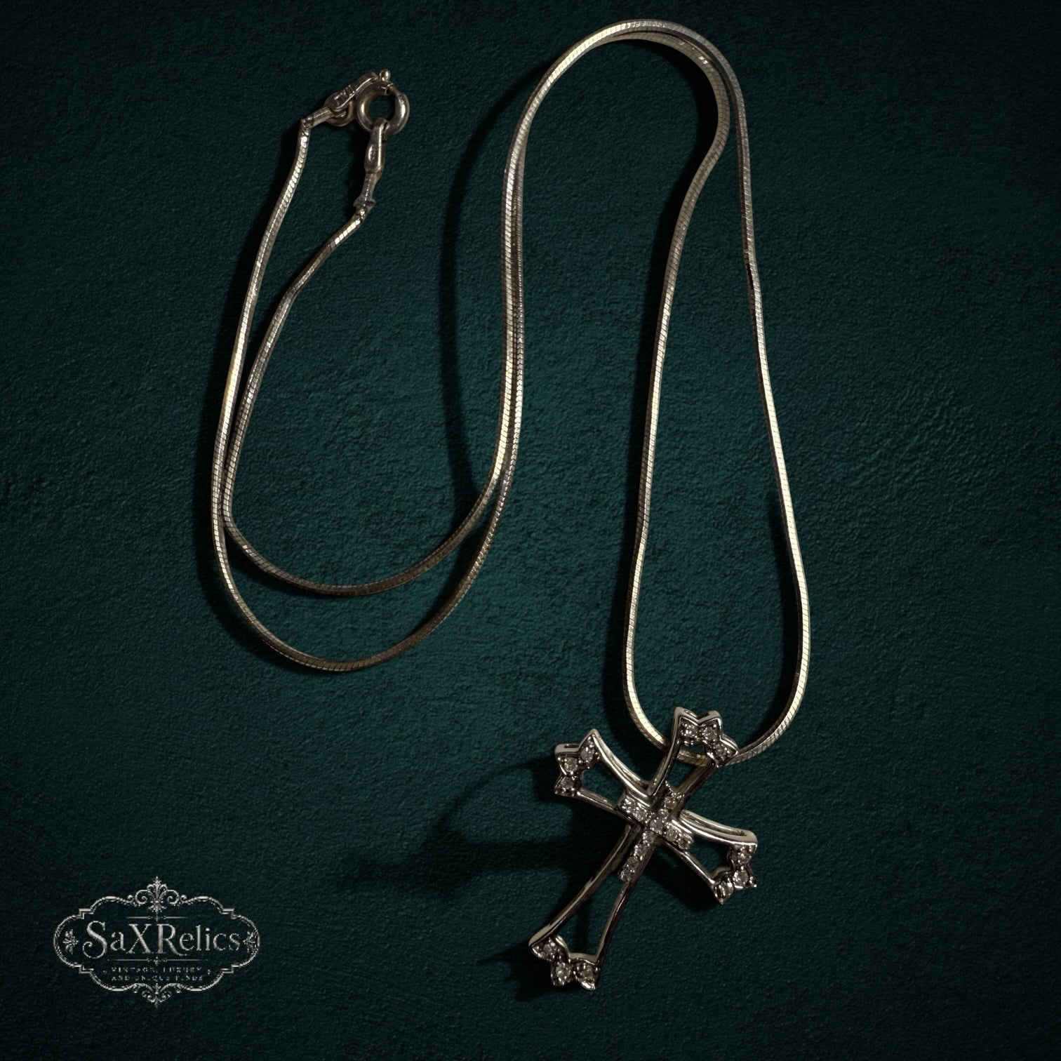 My Store sterling silver cross pendant necklace with clear stones on a sleek snake chain against a dark background.