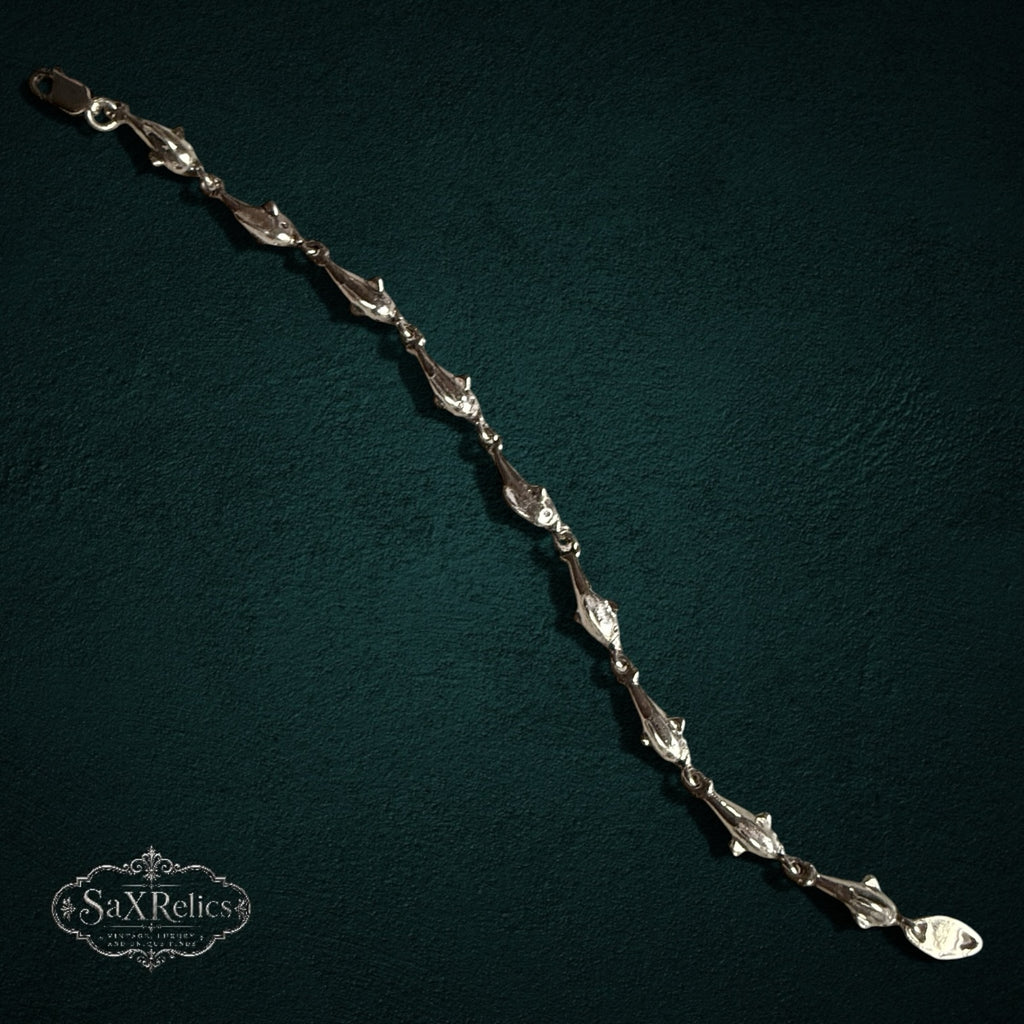 SaX Relics — Delfines sterling silver dolphin-link bracelet, polished links on a dark teal backdrop.