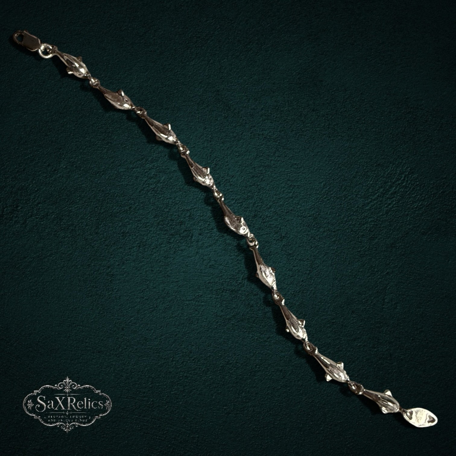 SaX Relics — Delfines sterling silver dolphin-link bracelet, polished links on a dark teal backdrop.