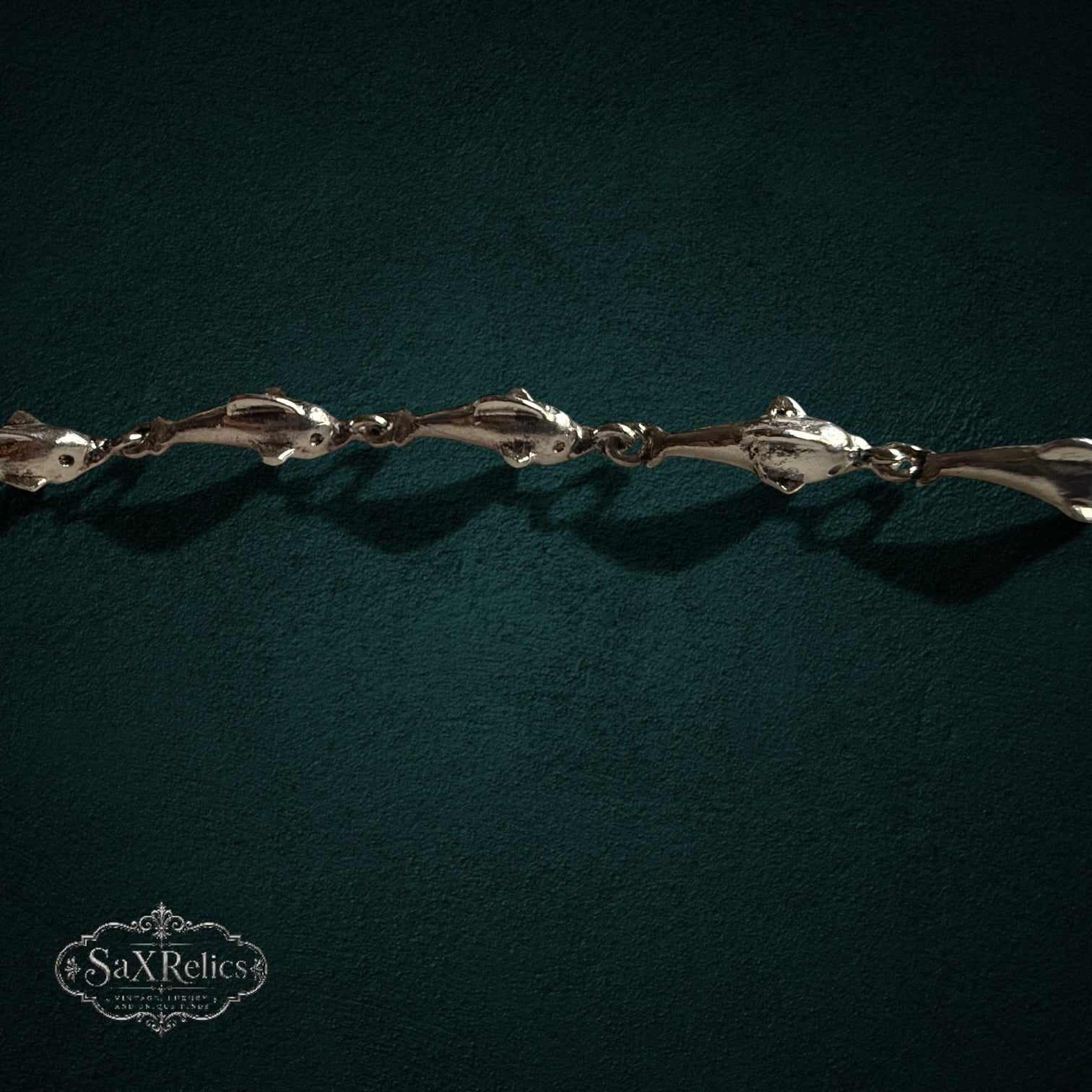 SaX Relics — Delfines sterling silver dolphin-link bracelet, full length shown on a dark teal backdrop.