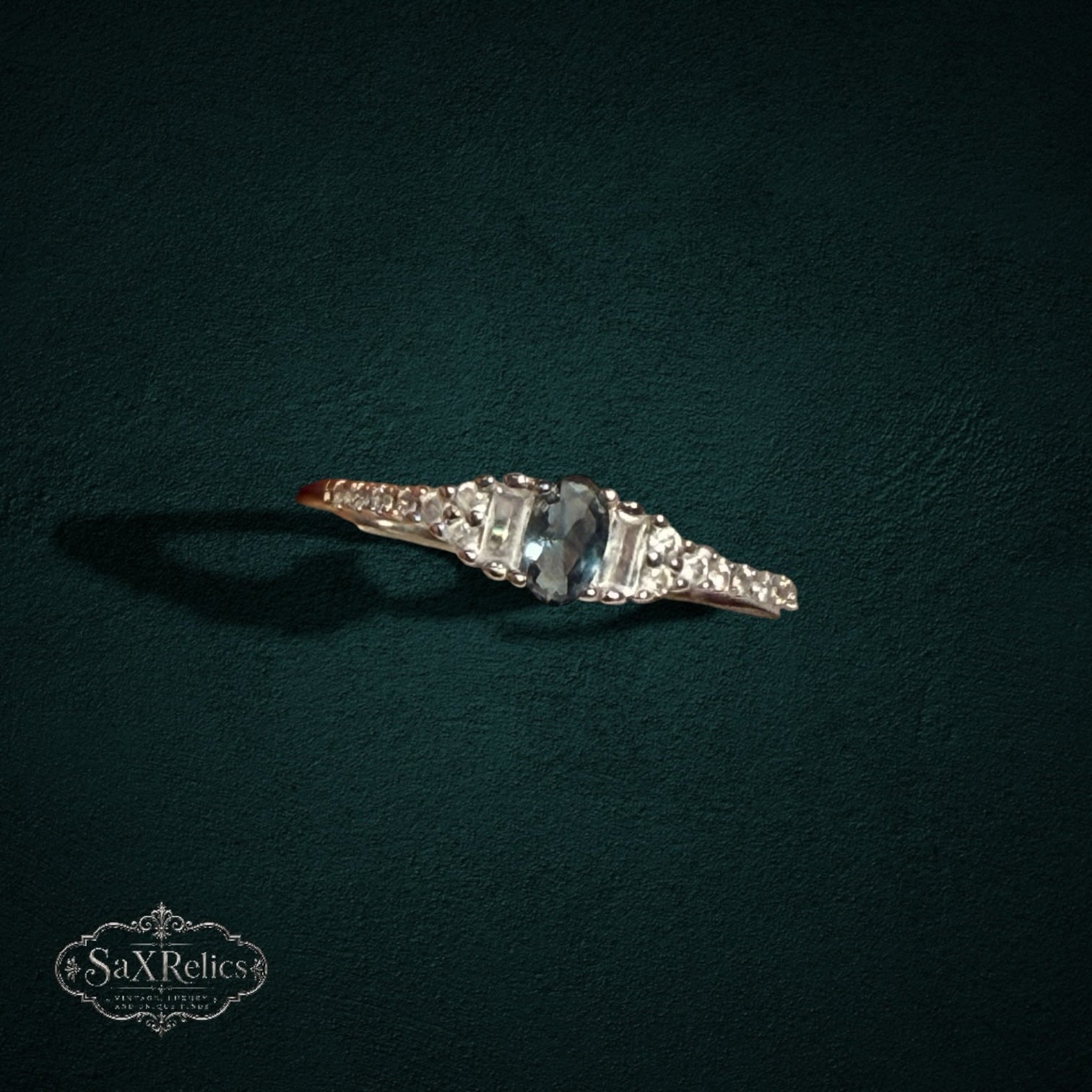 My Store sterling silver ring with a central oval gemstone, baguette accents, and round stones on a dark background.