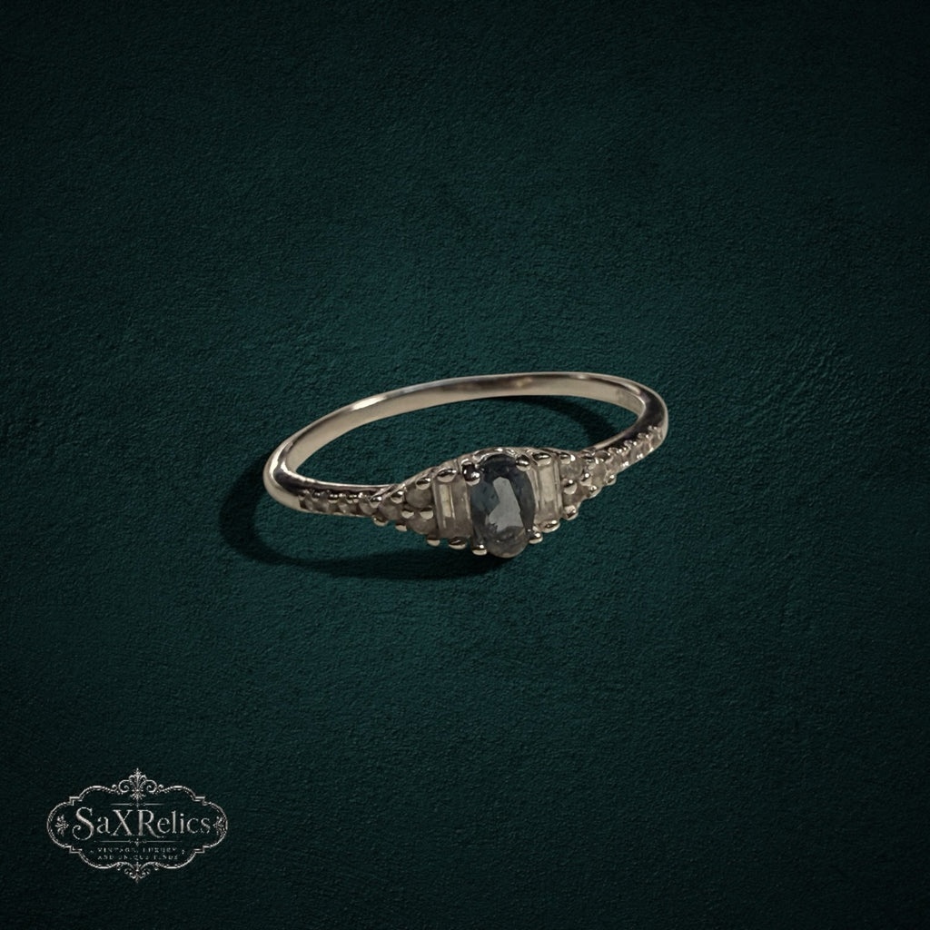 My Store sterling silver ring with a central oval gemstone, baguette accents, and round stones on a dark background.