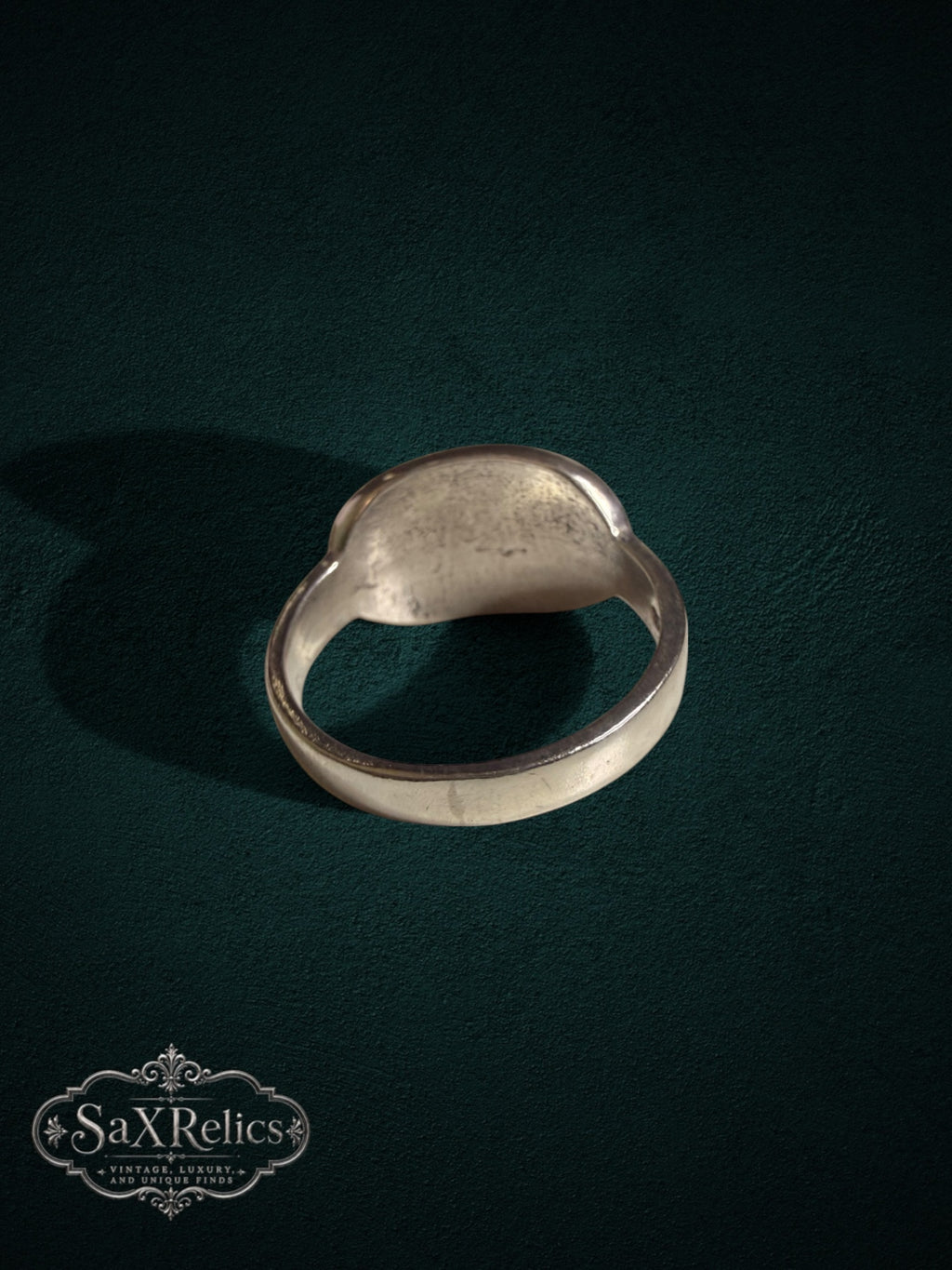 Sterling silver signet ring with a rustic finish, viewed from the back against a dark green background.