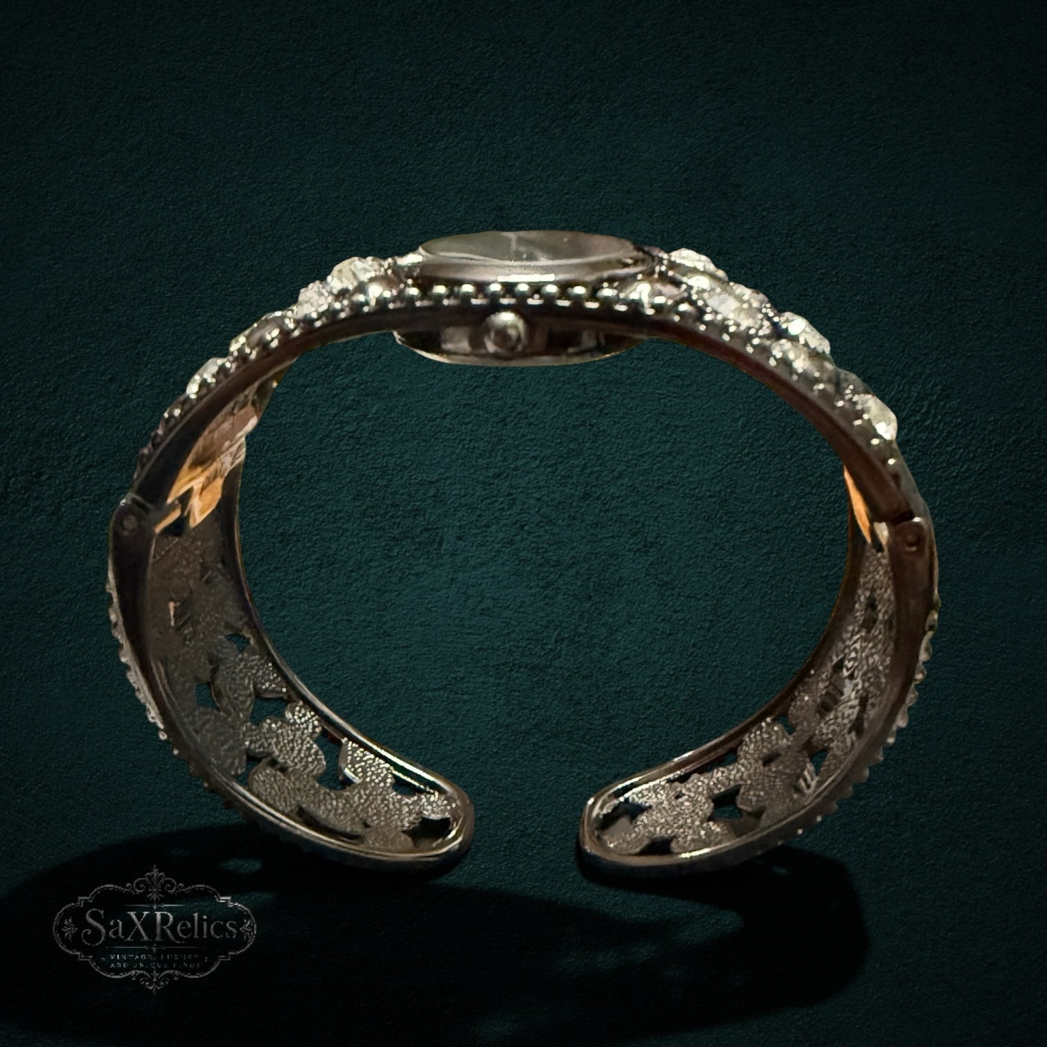 My Store STUDIO cuff watch in gunmetal with an ornate open-work band and crystal accents on a dark background.