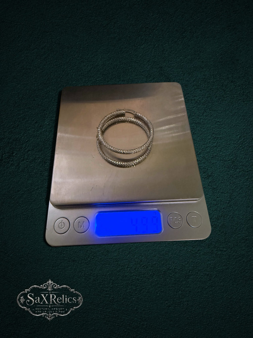 My Store SAXRelics textured silver hoop earrings with a diamond-cut finish resting on a digital scale.