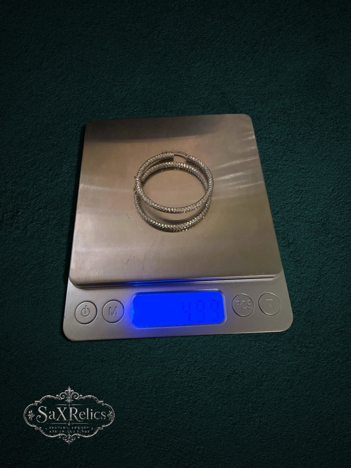 My Store SAXRelics textured silver hoop earrings with a diamond-cut finish resting on a digital scale.