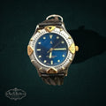 My Store vintage analog watch with a deep blue dial, two-tone silver and gold bezel, and dark brown leather strap.