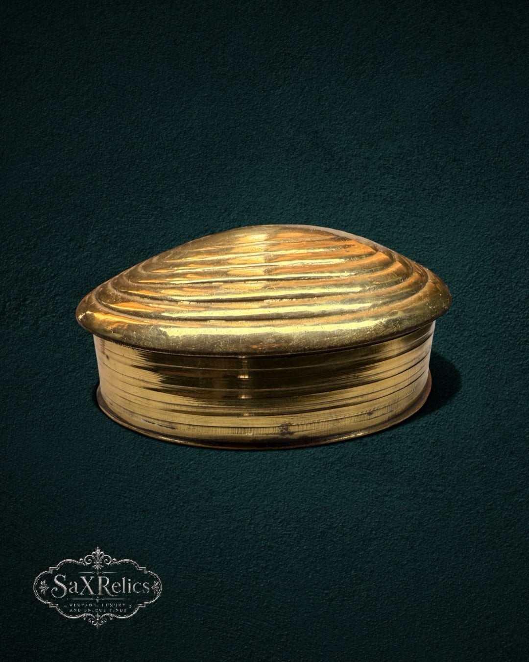 My Store vintage brass trinket box in a clam shell shape with embossed ridged lid details on a dark background.