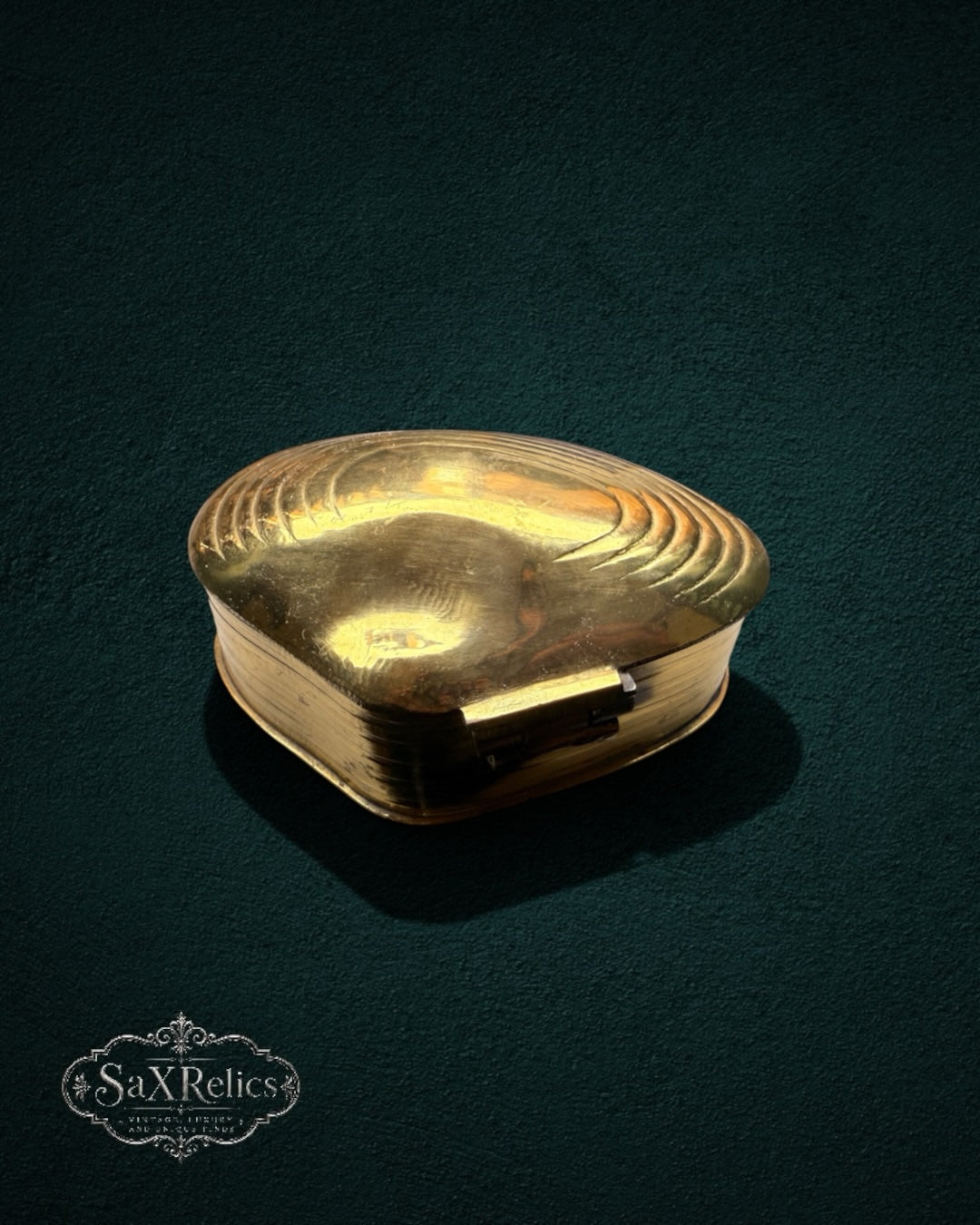 My Store vintage brass trinket box in a clam shell shape with embossed ridged lid details on a dark green background.