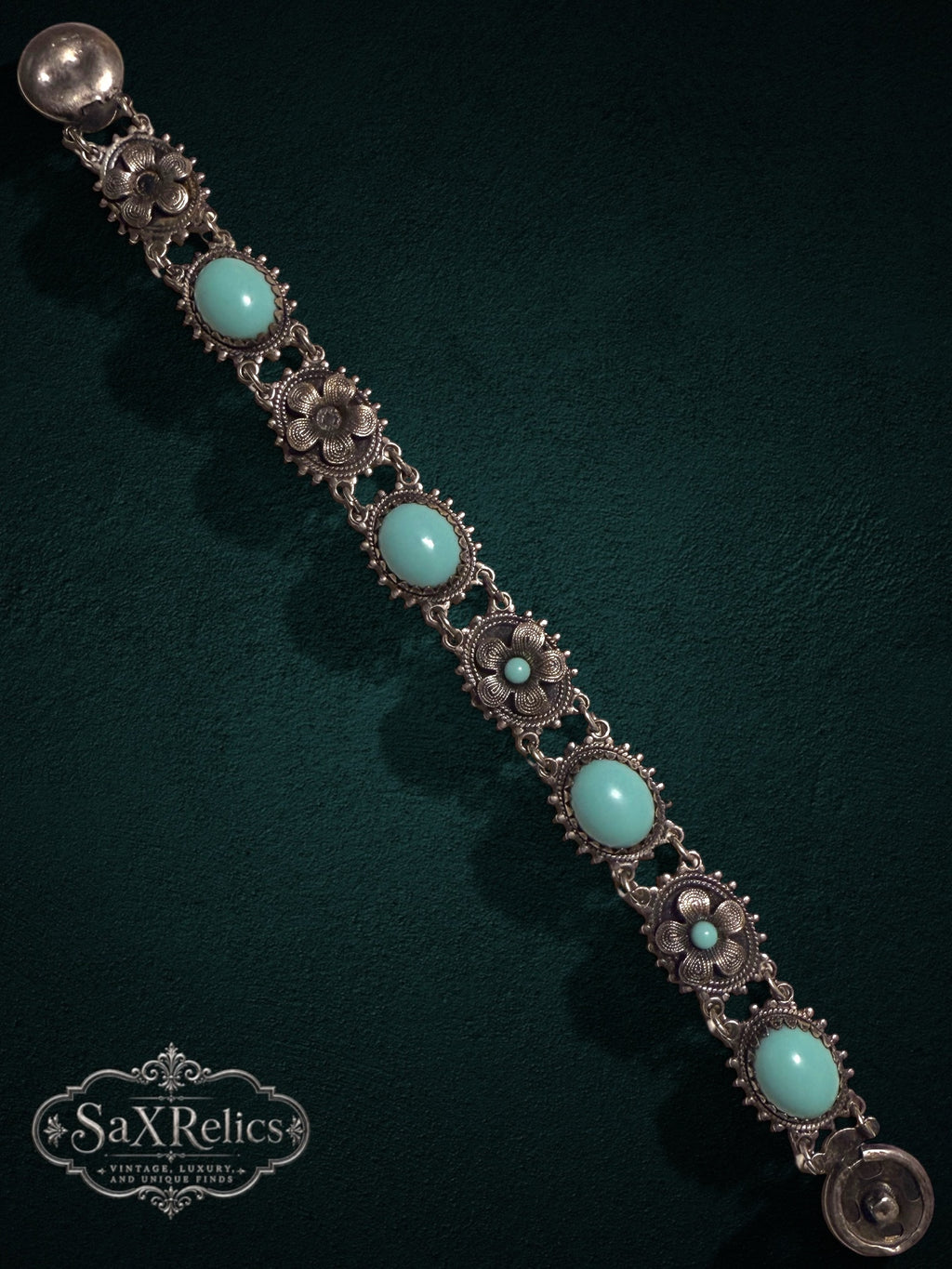 Vintage style floral link bracelet with turquoise cabochons and aged silver filigree on a dark background