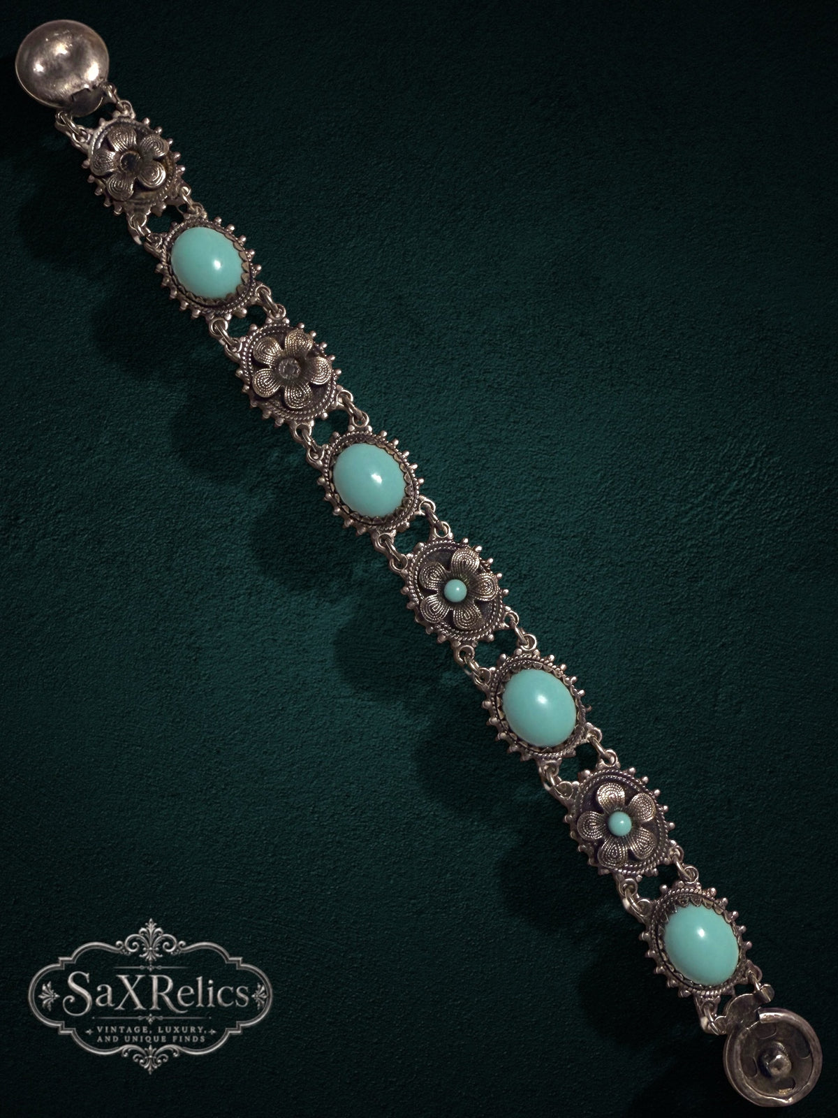 Vintage style floral link bracelet with turquoise cabochons and aged silver filigree on a dark background