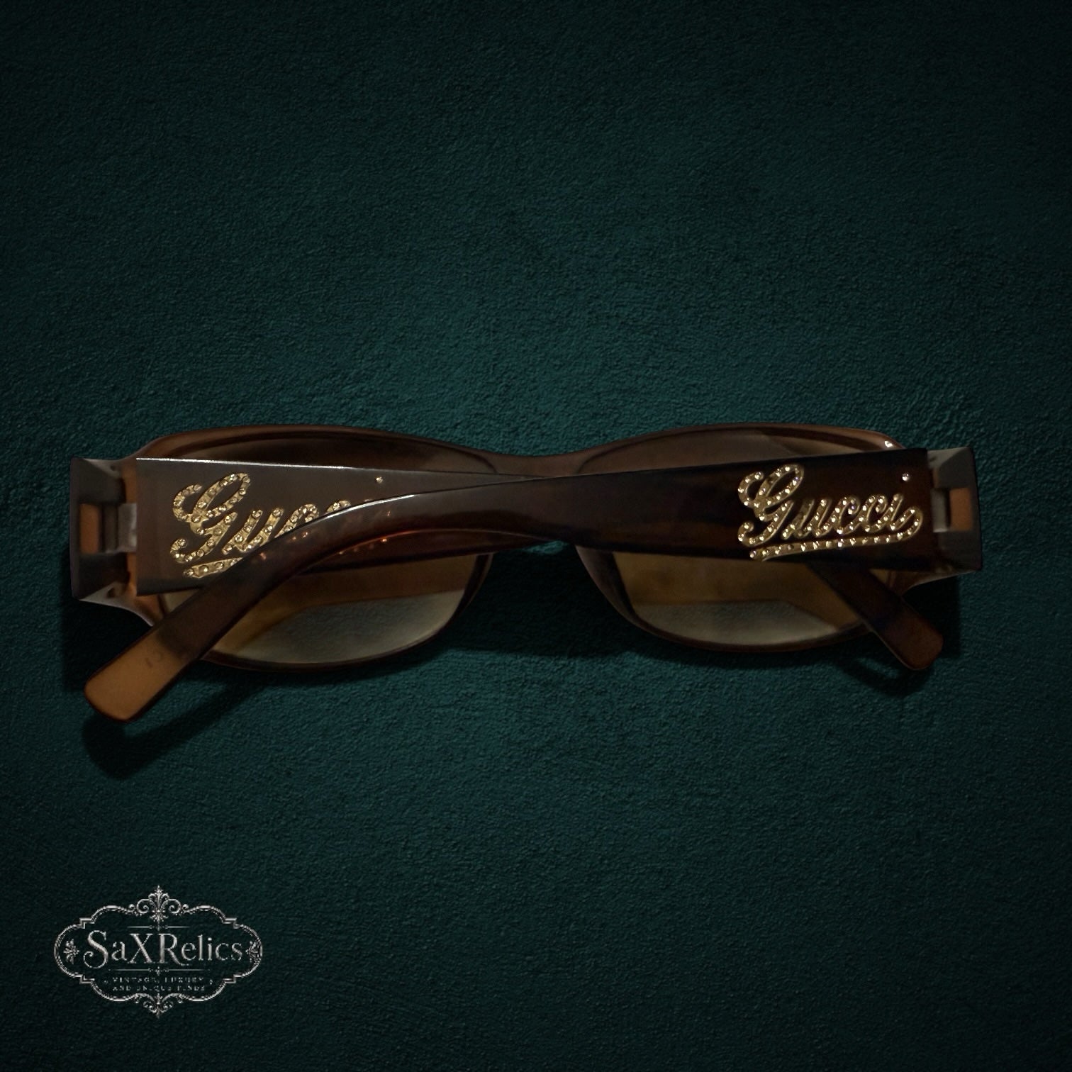 My Store vintage brown Gucci sunglasses with crystal-embellished logo on temples, displayed on a dark green surface.