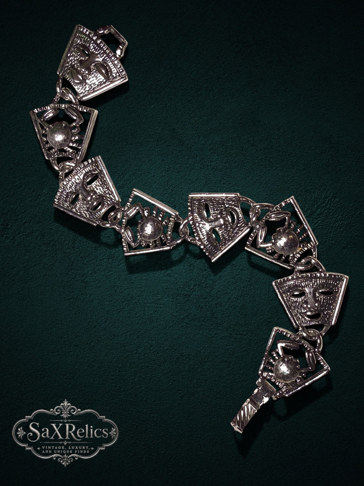 Vintage theatrical mask and crab link bracelet in polished silver-tone metal on a dark green background.