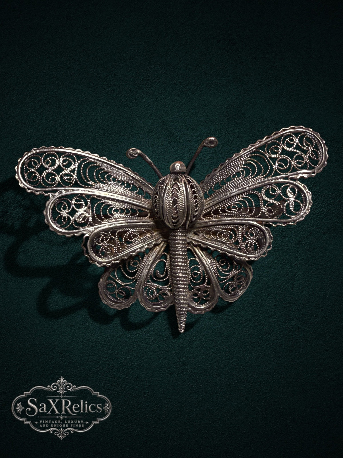 My Store vintage silver filigree butterfly brooch featuring intricate wirework patterns on a dark green background.